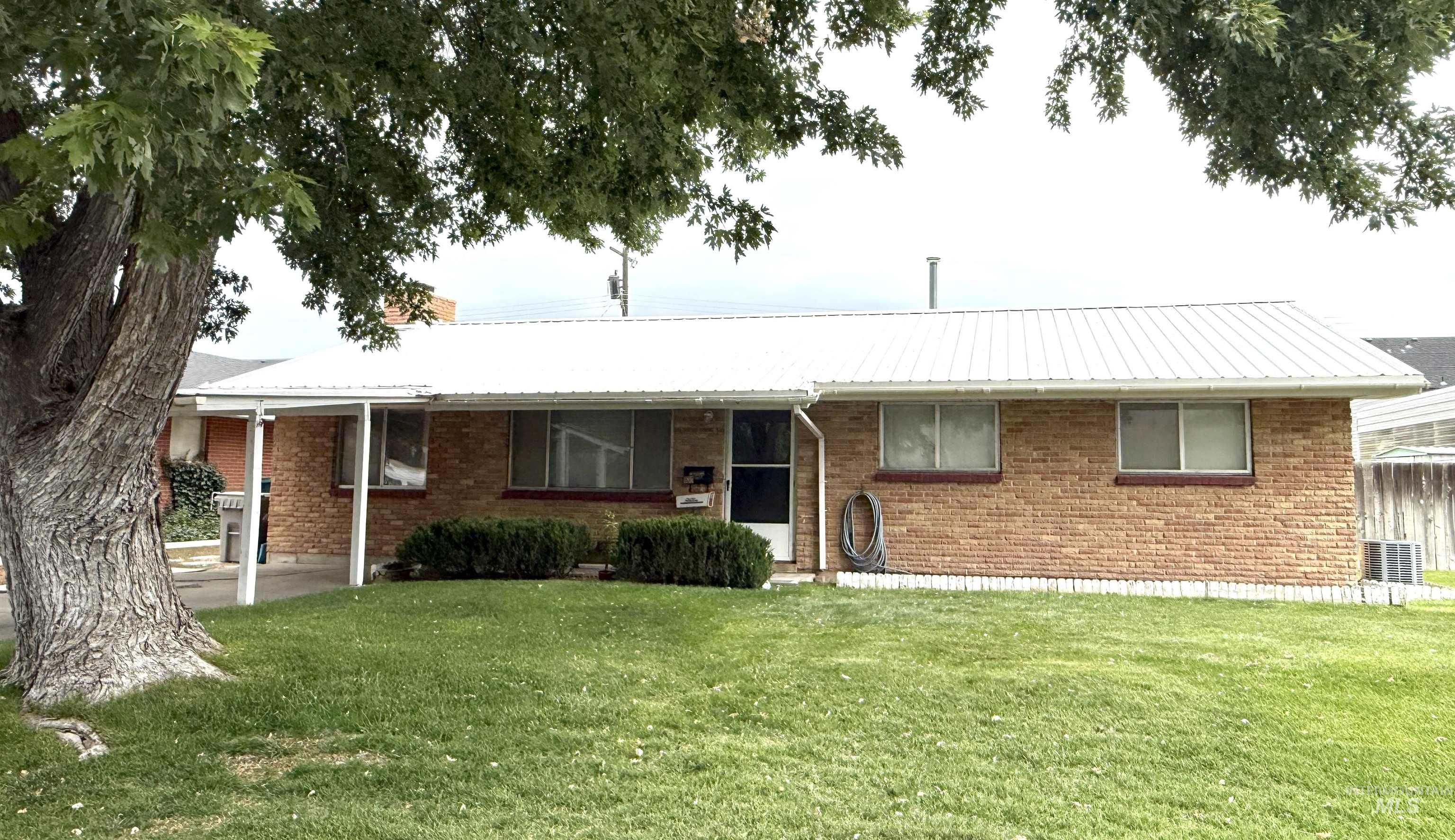 Ranch-style home featuring a metal roof, a front yard, brick siding, and a porch