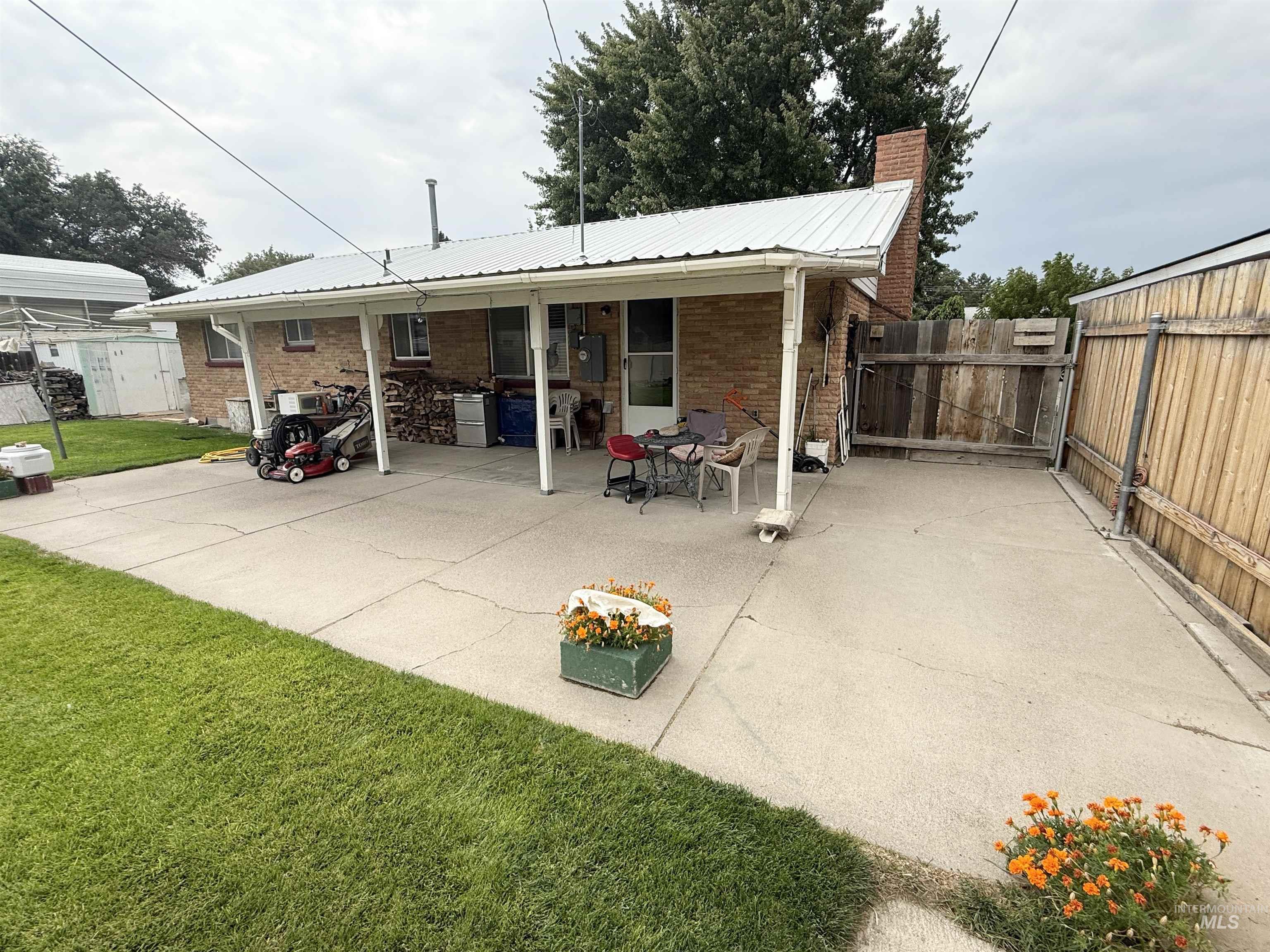 Back of house with a chimney, a patio, brick siding, and a metal roof