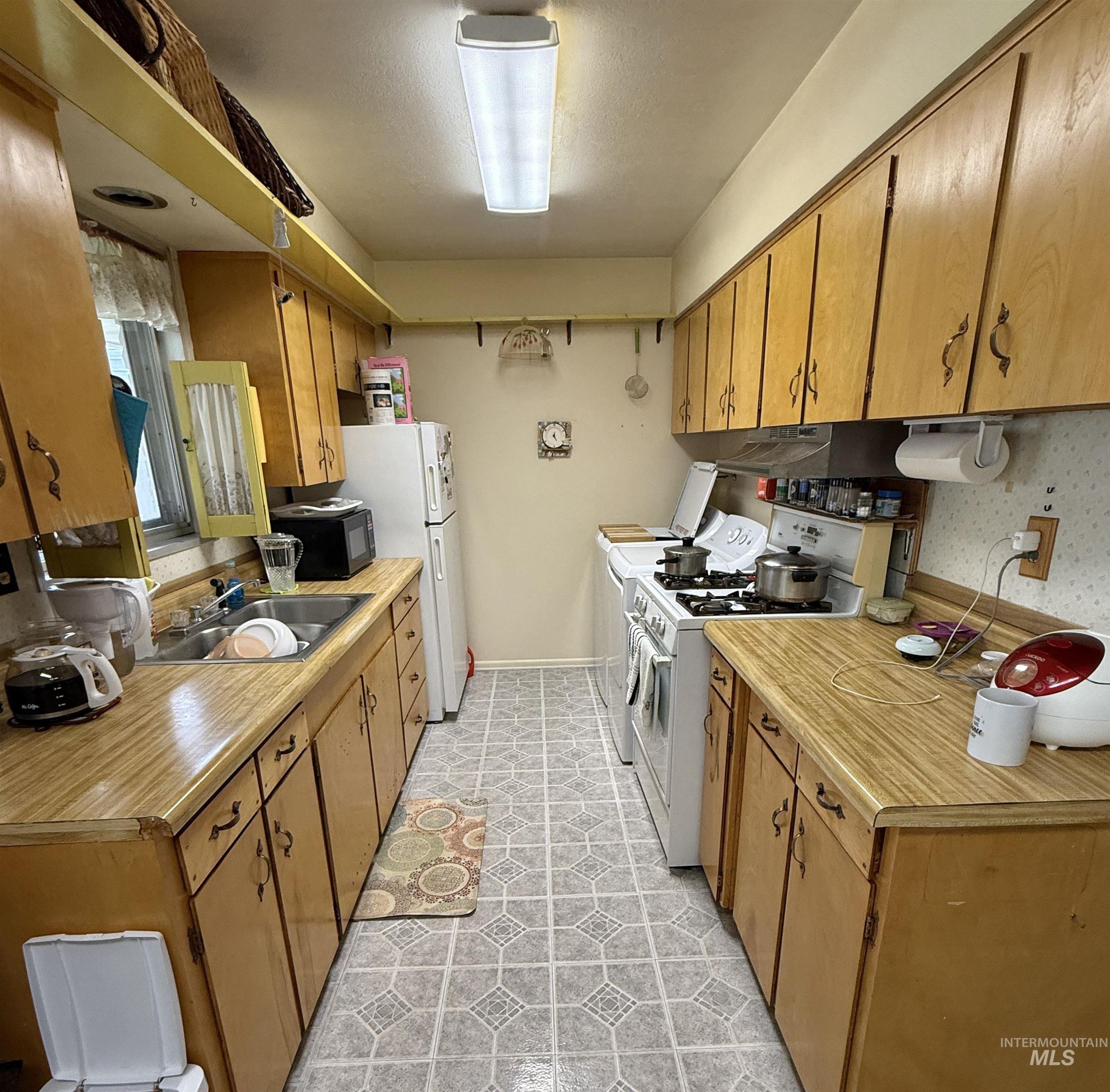 Kitchen with white appliances, light countertops, under cabinet range hood, and brown cabinets