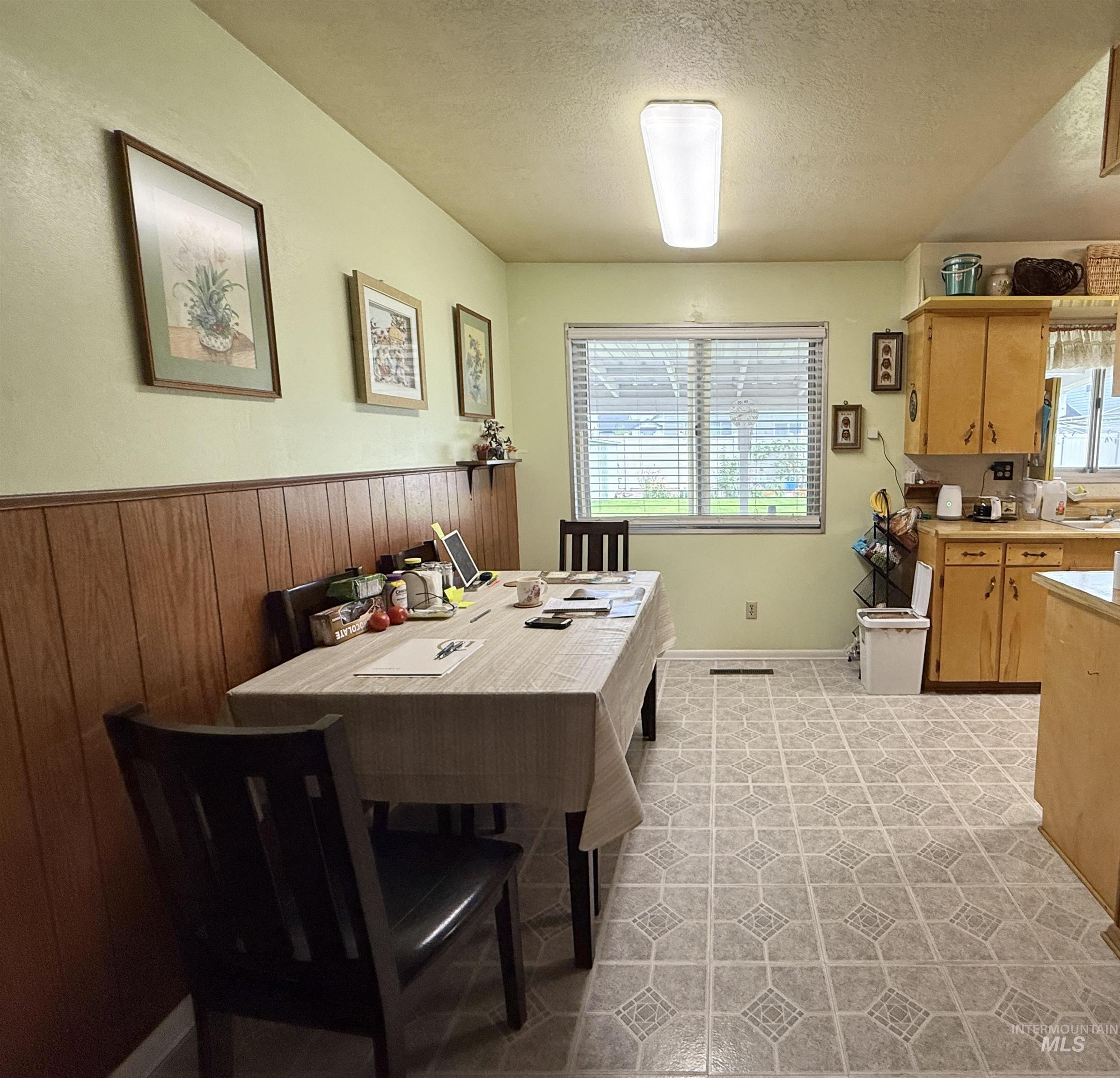 Dining room with a textured ceiling, wood walls, and light tile patterned floors