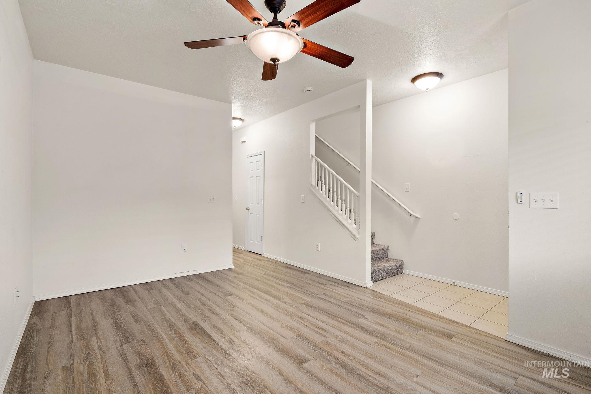 Unfurnished living room with stairway, light wood finished floors, a ceiling fan, and a textured ceiling