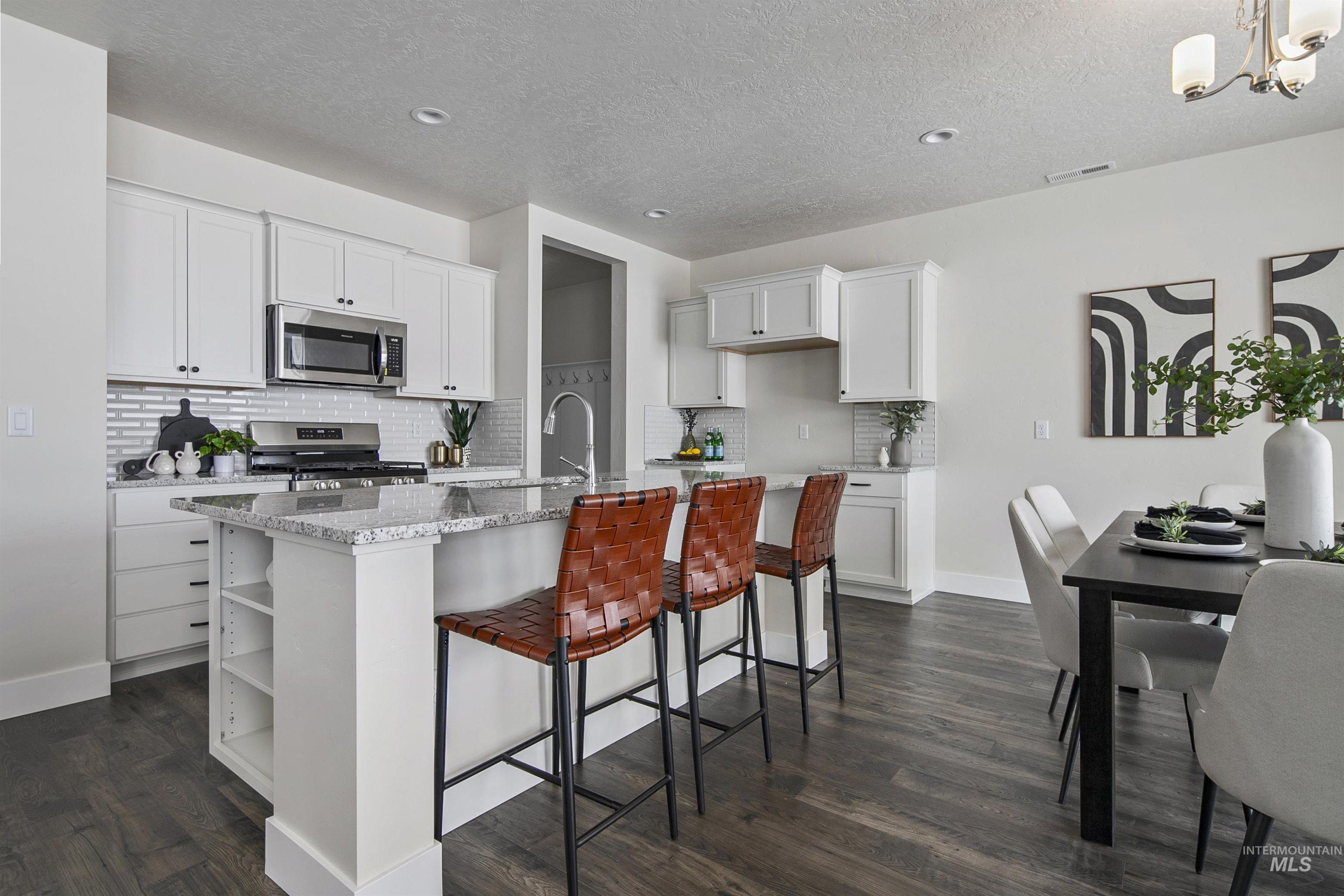 Kitchen with light stone counters, white cabinets, a breakfast bar area, decorative backsplash, and an island with sink