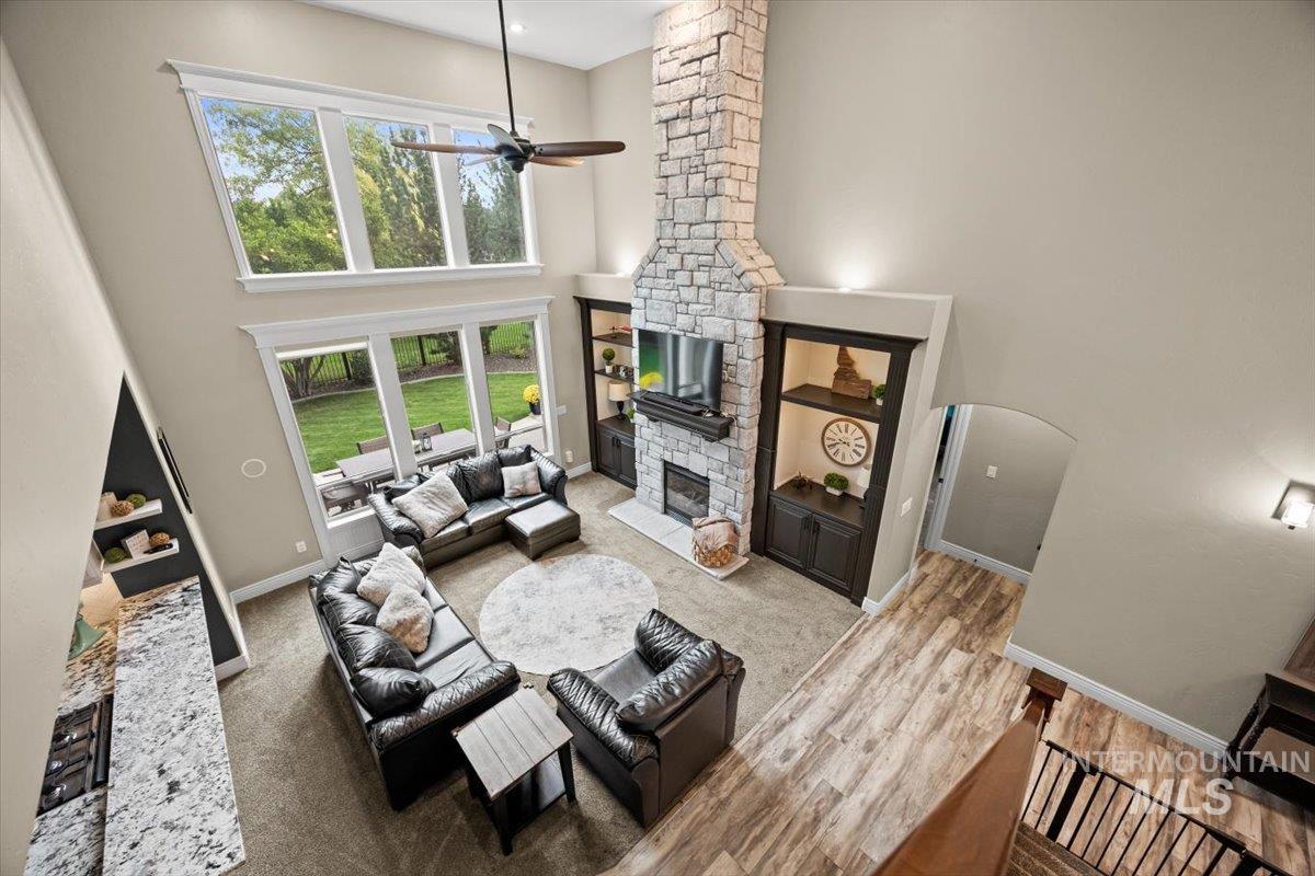 Living area with a stone fireplace, a towering ceiling, ceiling fan, wood finished floors, and arched walkways