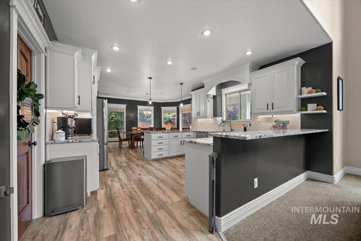 Kitchen with light stone countertops, pendant lighting, backsplash, white cabinets, and a peninsula