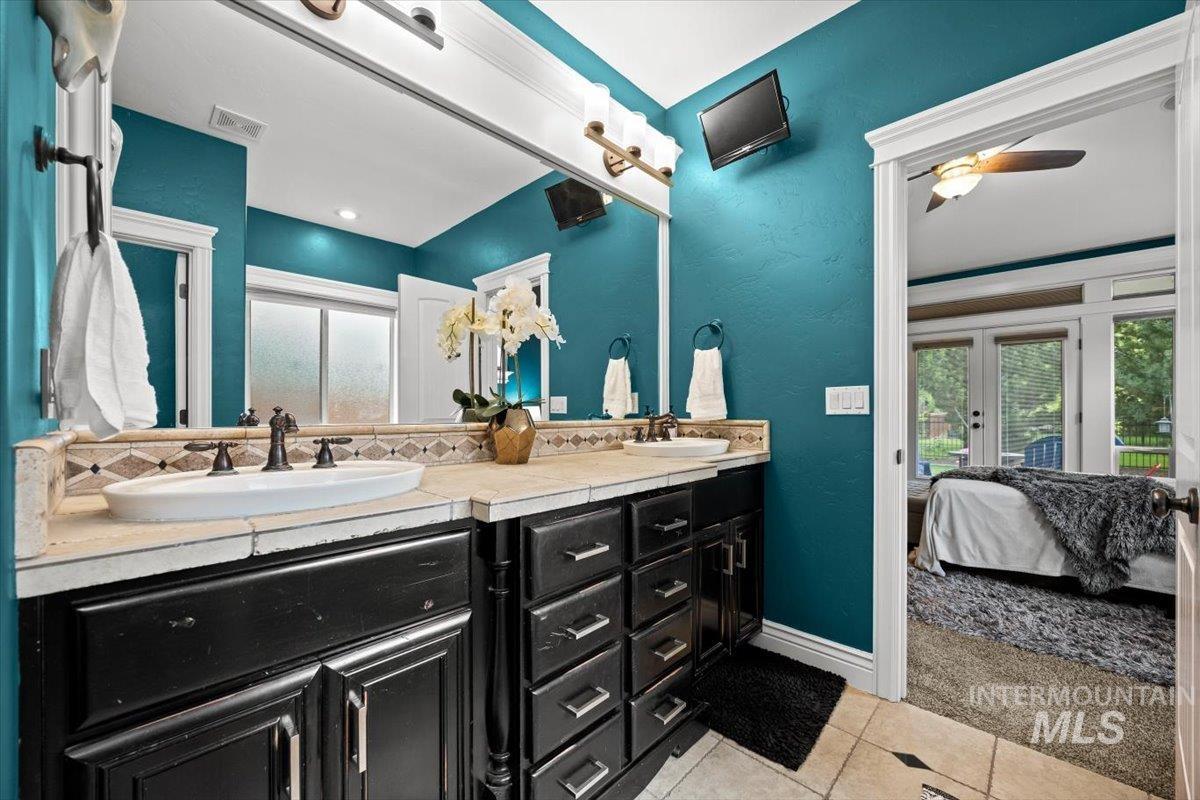 Ensuite bathroom featuring light tile patterned floors, double vanity, a ceiling fan, and a textured wall