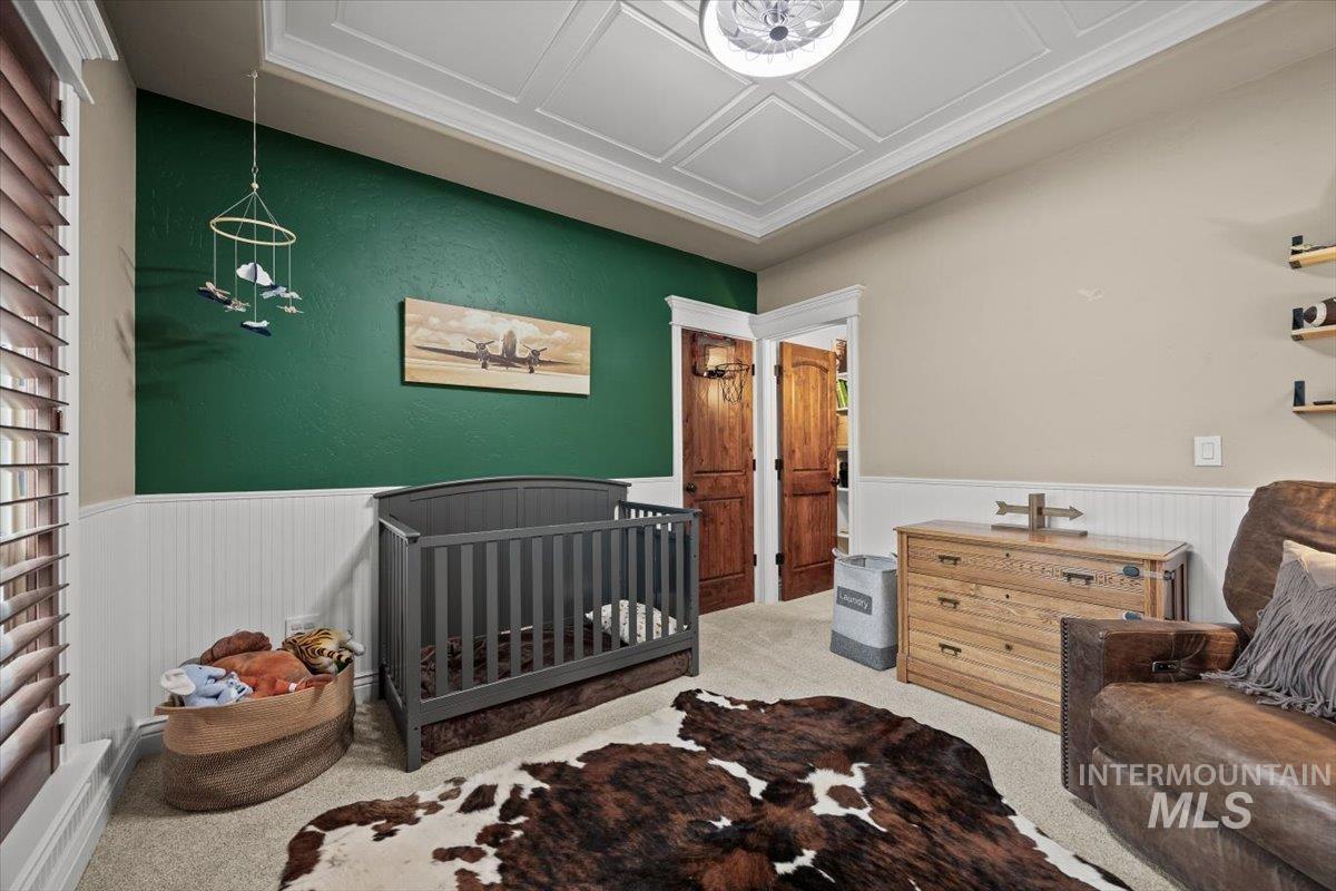 Carpeted bedroom featuring a nursery area and wainscoting