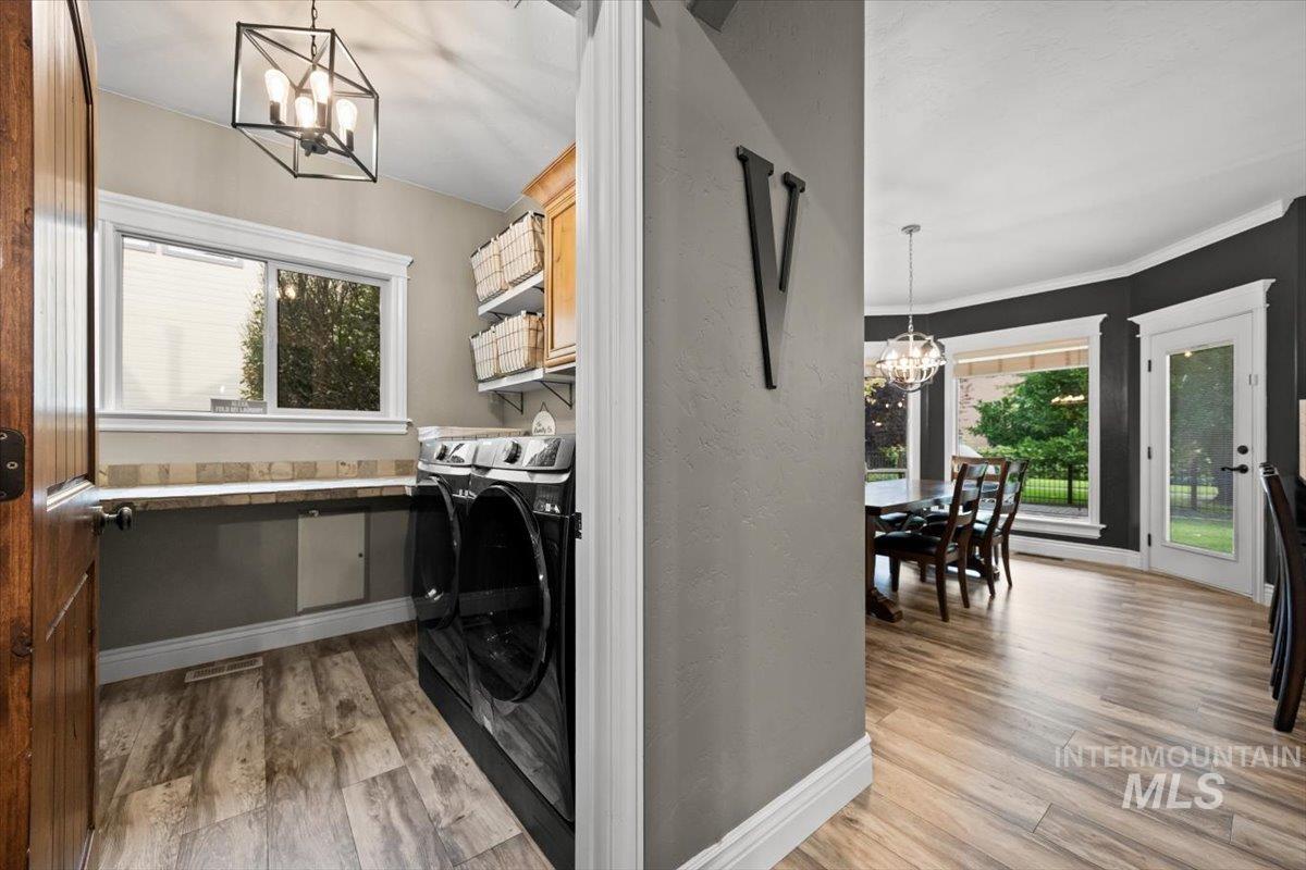 Washroom with a chandelier, light wood finished floors, plenty of natural light, washing machine and dryer, and a textured wall