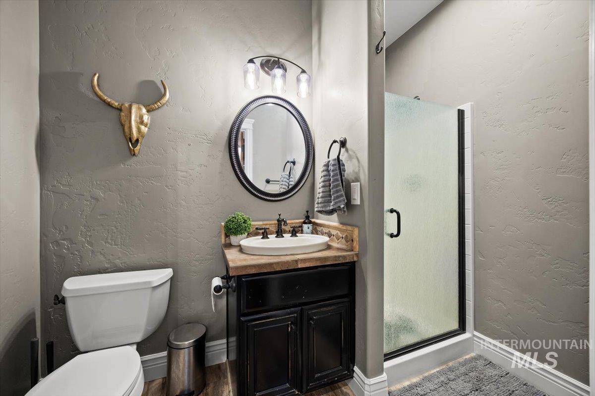 Full bath with a textured wall, a shower stall, vanity, and dark wood-style floors