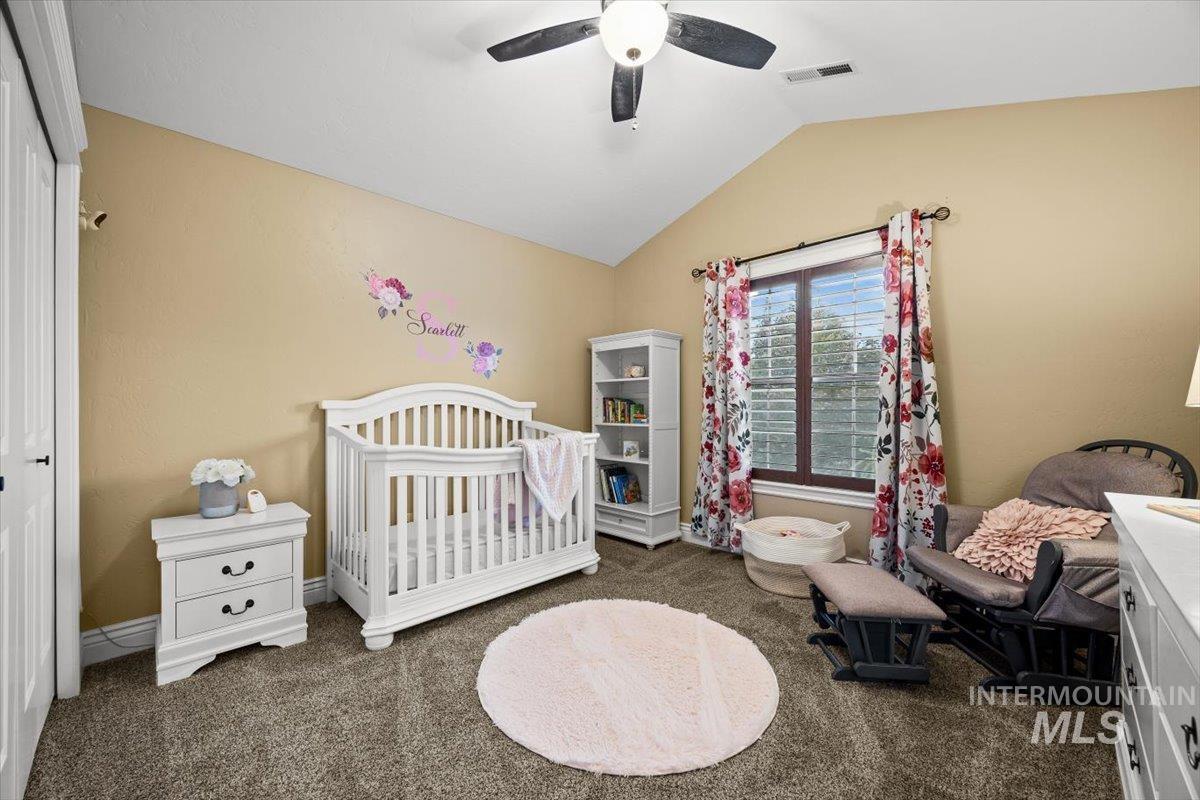 Bedroom featuring dark colored carpet, a nursery area, vaulted ceiling, and a ceiling fan
