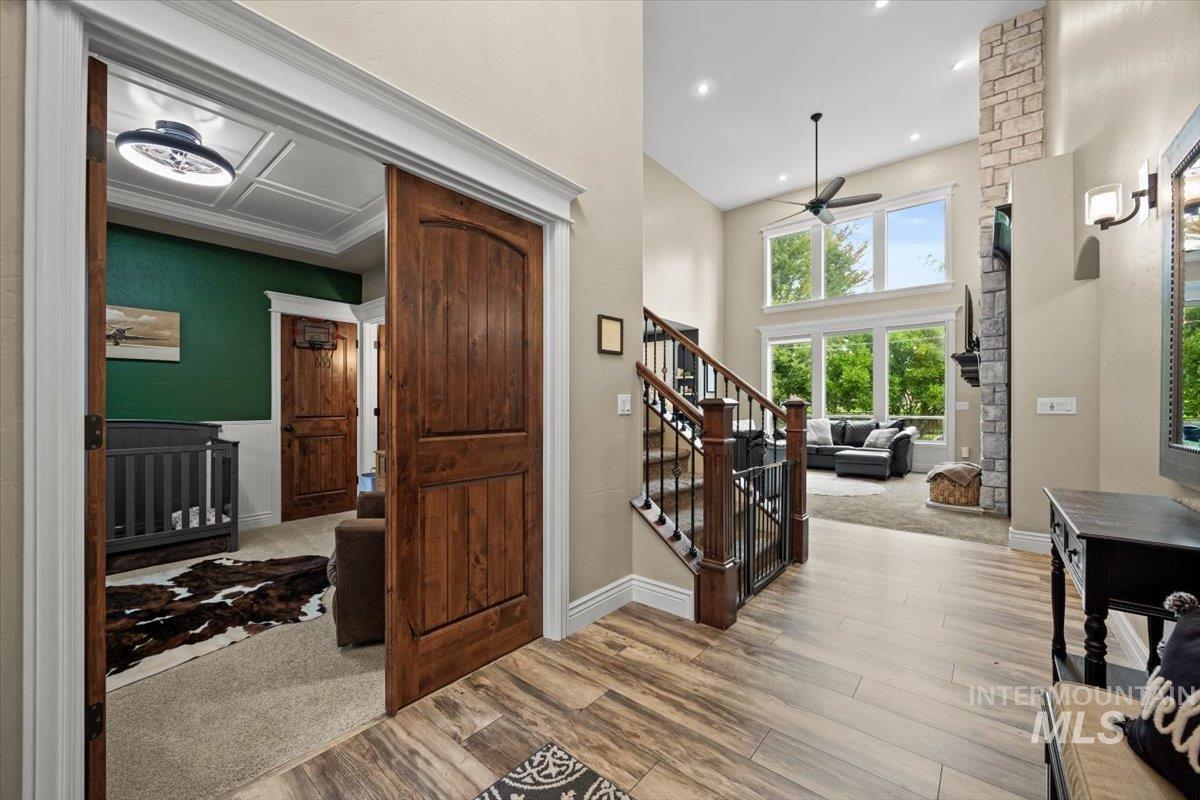 Entryway with ceiling fan, stairway, light colored carpet, light wood finished floors, and a high ceiling