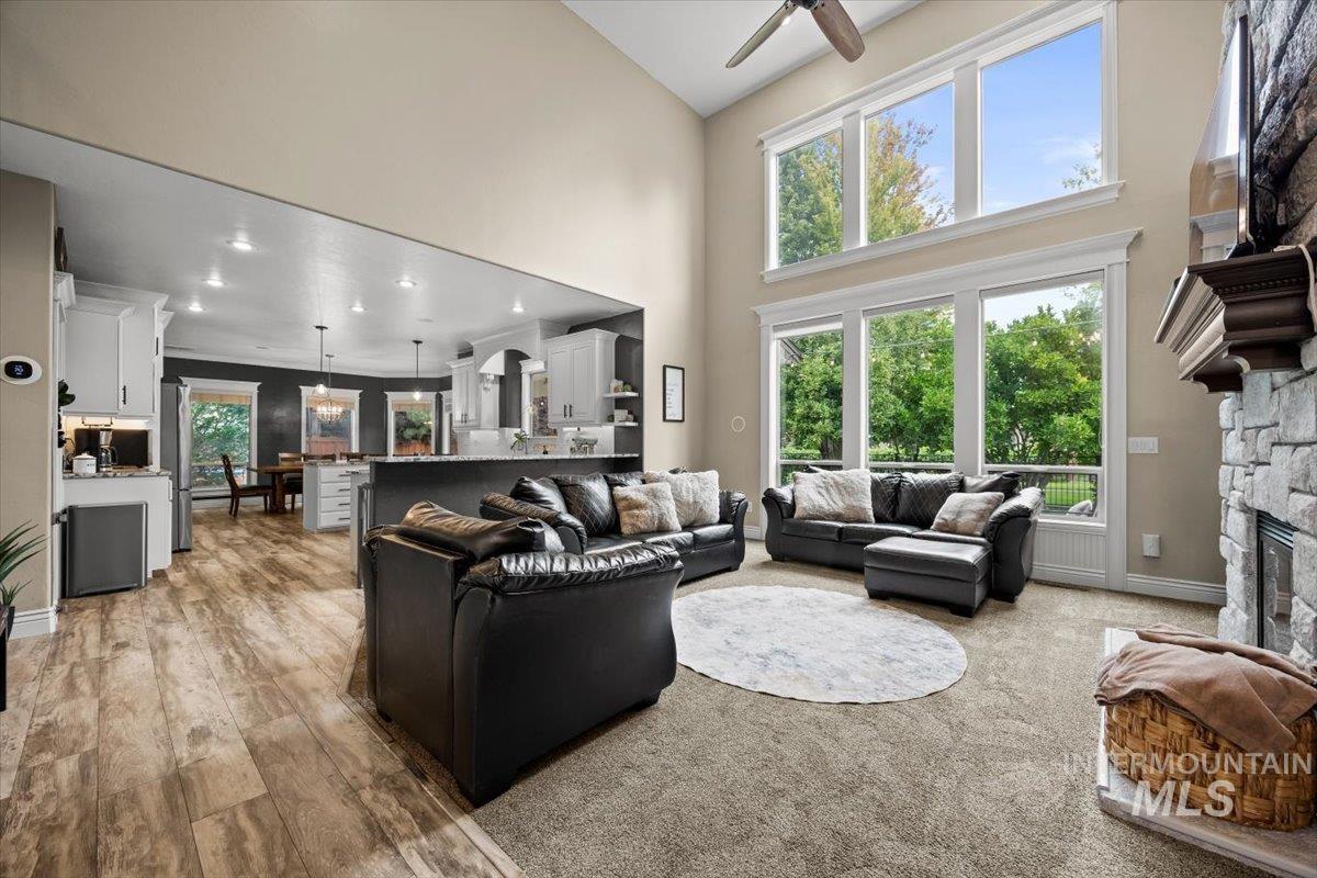 Living room with a fireplace, a high ceiling, light colored carpet, and a ceiling fan