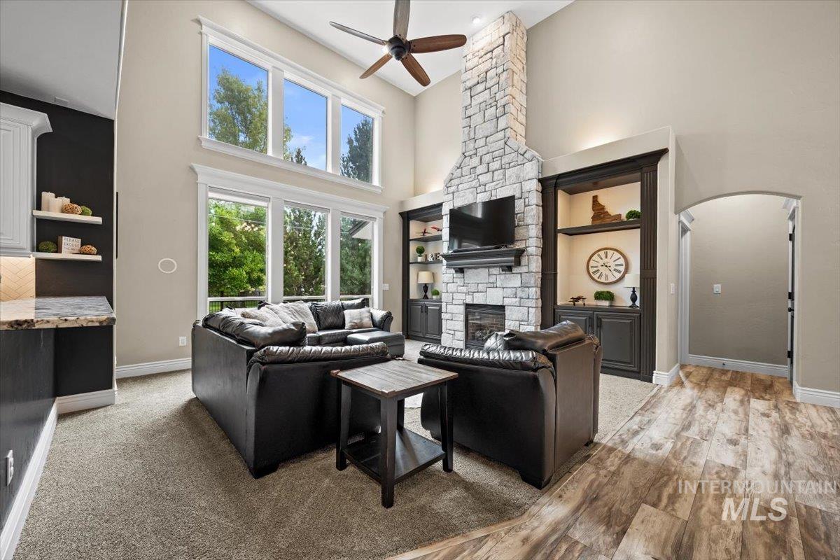 Living area featuring a towering ceiling, a ceiling fan, a fireplace, arched walkways, and light wood-style flooring