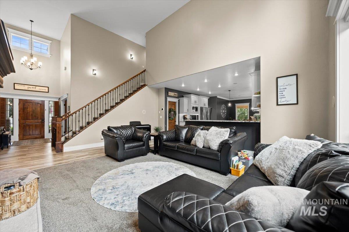 Living room with a high ceiling, plenty of natural light, stairs, a chandelier, and wood finished floors