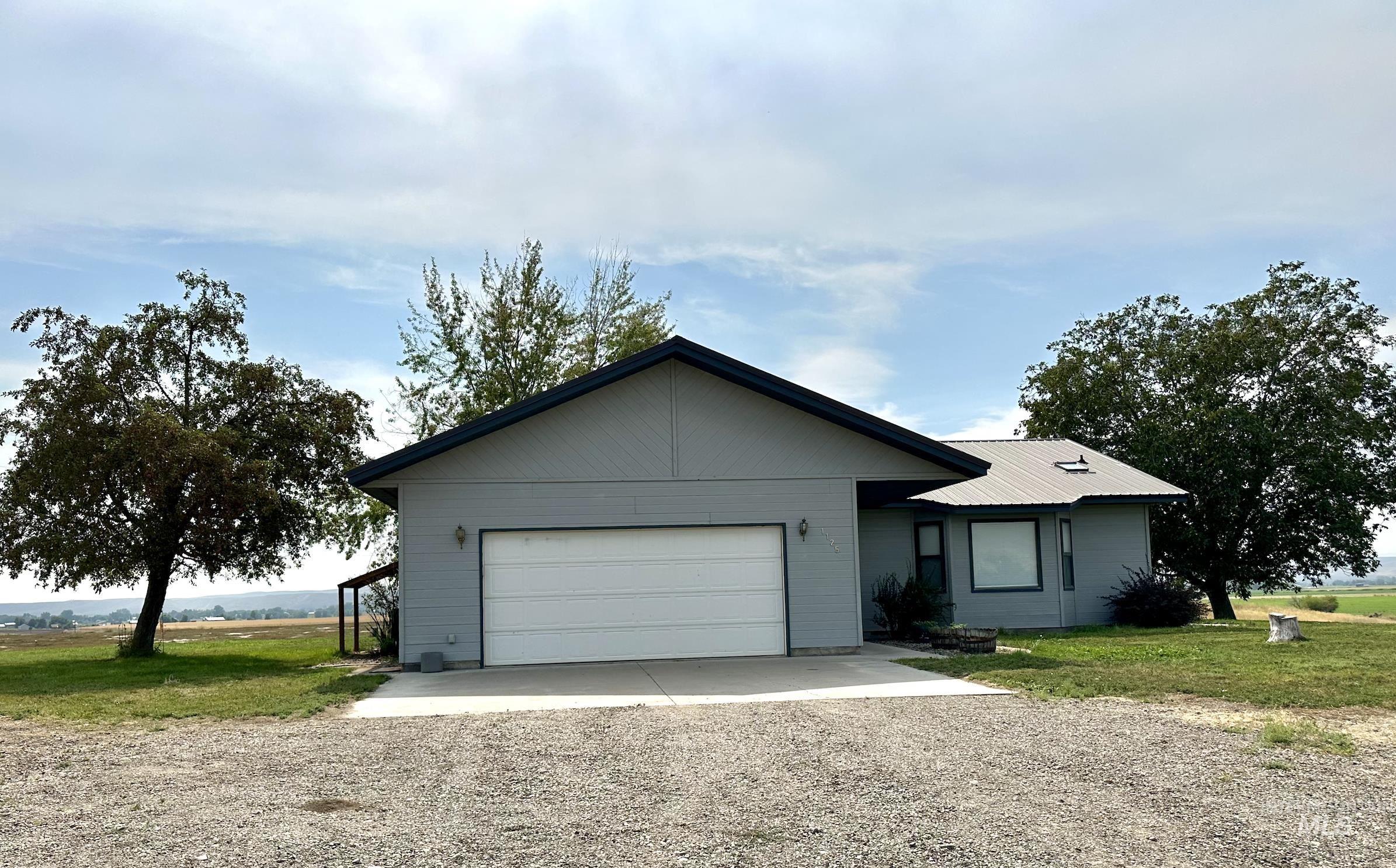 Ranch-style house with gravel driveway, a front lawn, an attached garage, and a metal roof