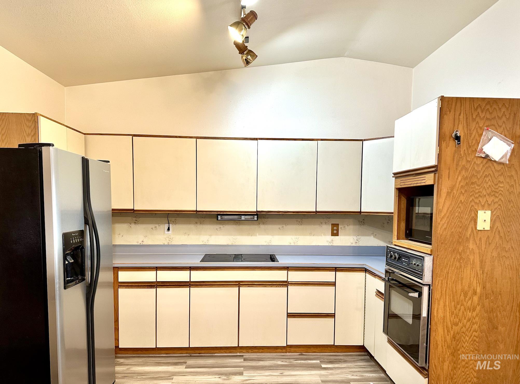 Kitchen featuring black appliances, light countertops, lofted ceiling, and light wood-style floors