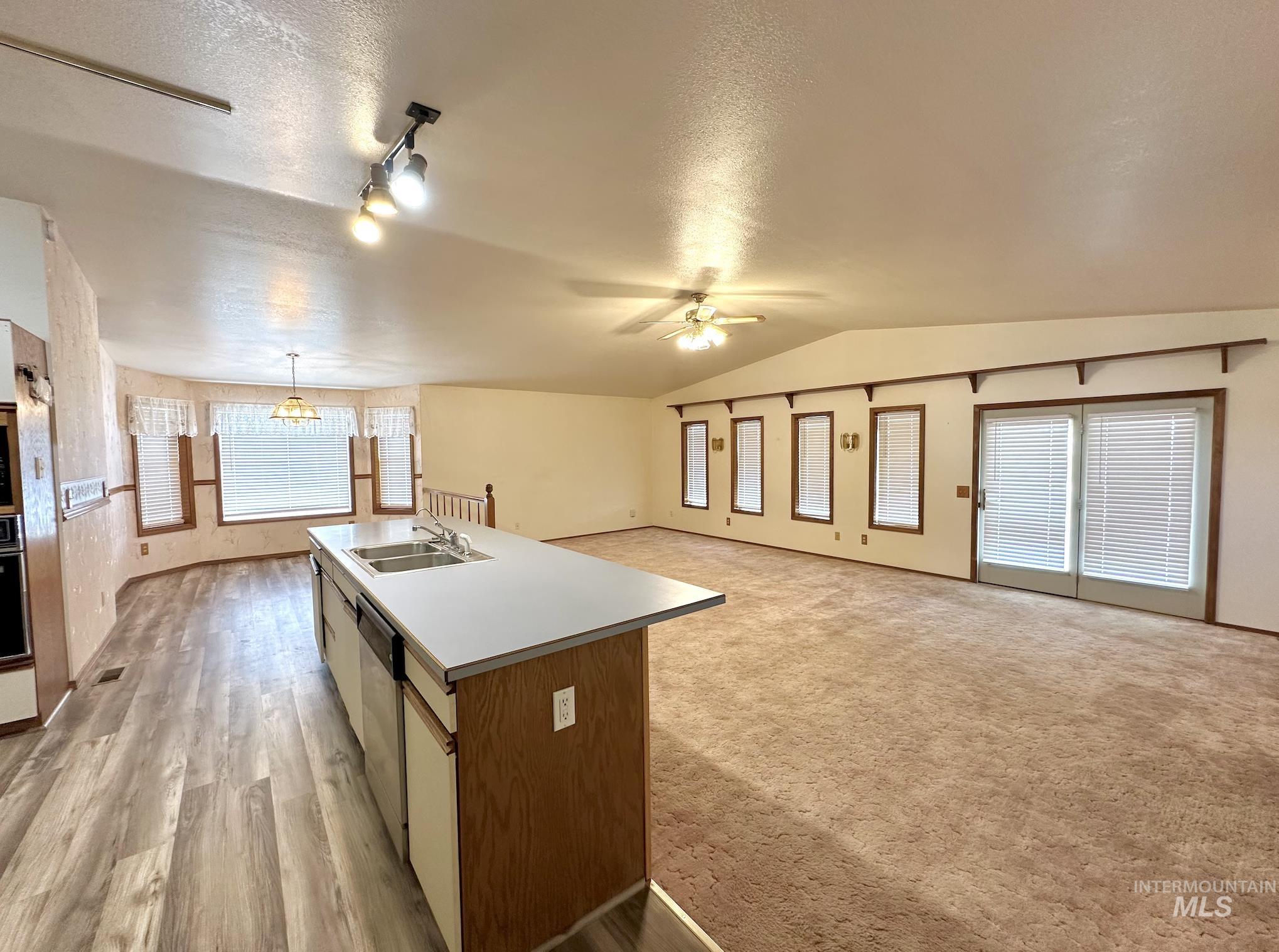 Kitchen with open floor plan, a textured ceiling, light countertops, vaulted ceiling, and a center island with sink