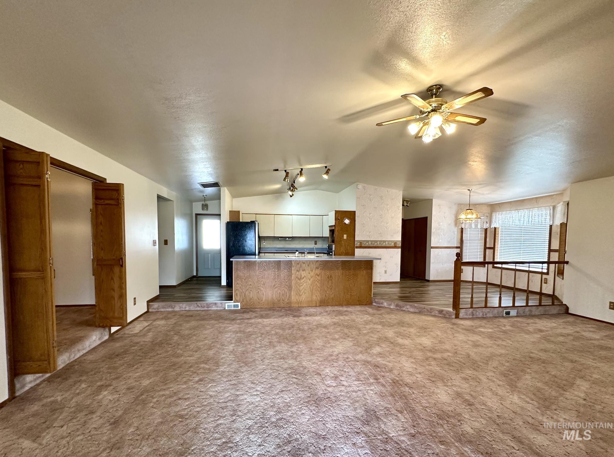Kitchen with open floor plan, lofted ceiling, dark colored carpet, a ceiling fan, and a kitchen island