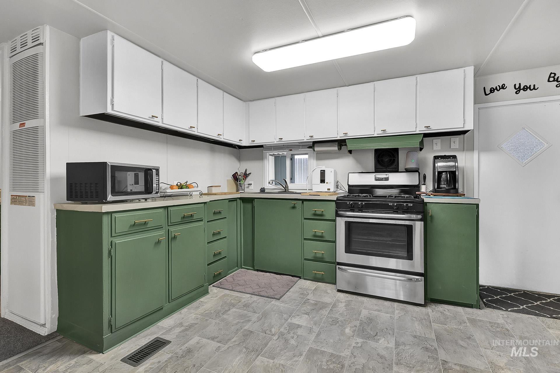 Kitchen featuring green cabinetry, appliances with stainless steel finishes, white cabinets, and light countertops