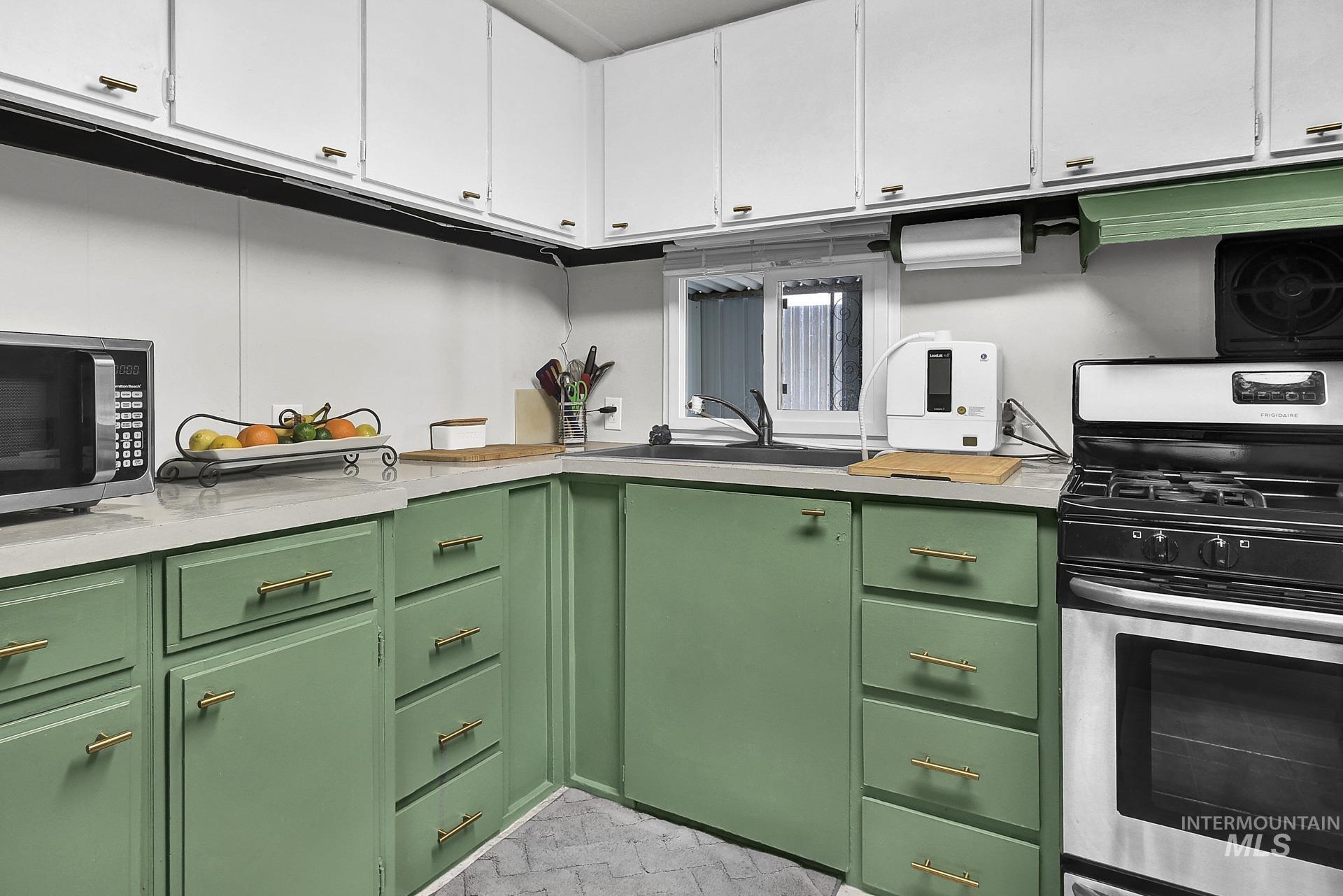Kitchen featuring green cabinetry, appliances with stainless steel finishes, light countertops, white cabinets, and exhaust hood