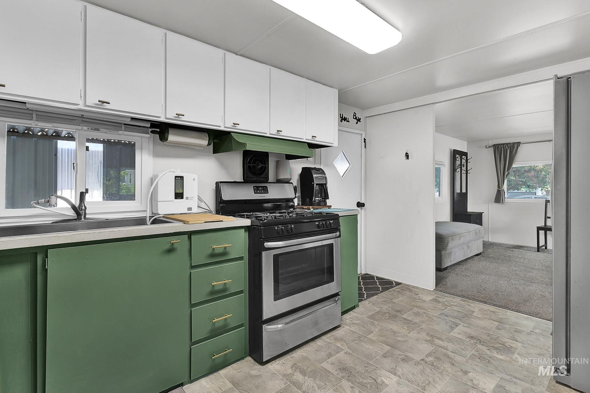 Kitchen with green cabinets, appliances with stainless steel finishes, light countertops, stone finish flooring, and custom exhaust hood