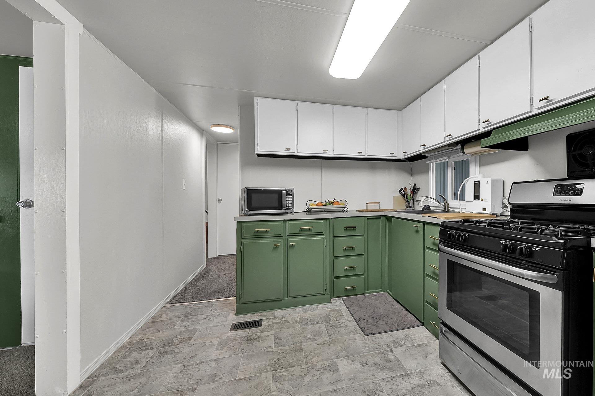 Kitchen featuring stainless steel appliances, green cabinetry, white cabinetry, light countertops, and stone finish floors