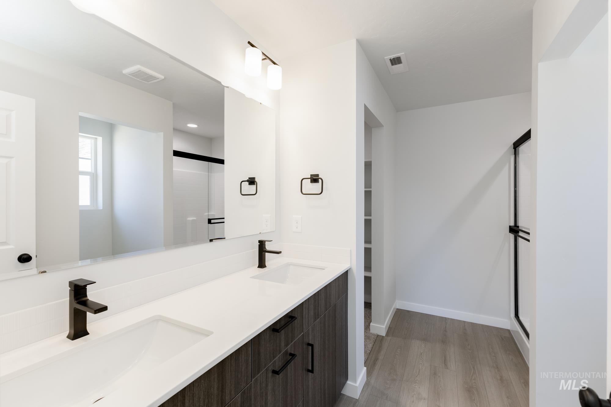 Bathroom featuring wood finished floors, a shower with shower door, double vanity, and a walk in closet