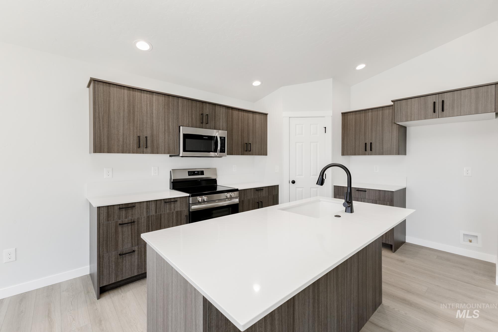 Kitchen with vaulted ceiling, stainless steel appliances, modern cabinets, light countertops, and a center island with sink