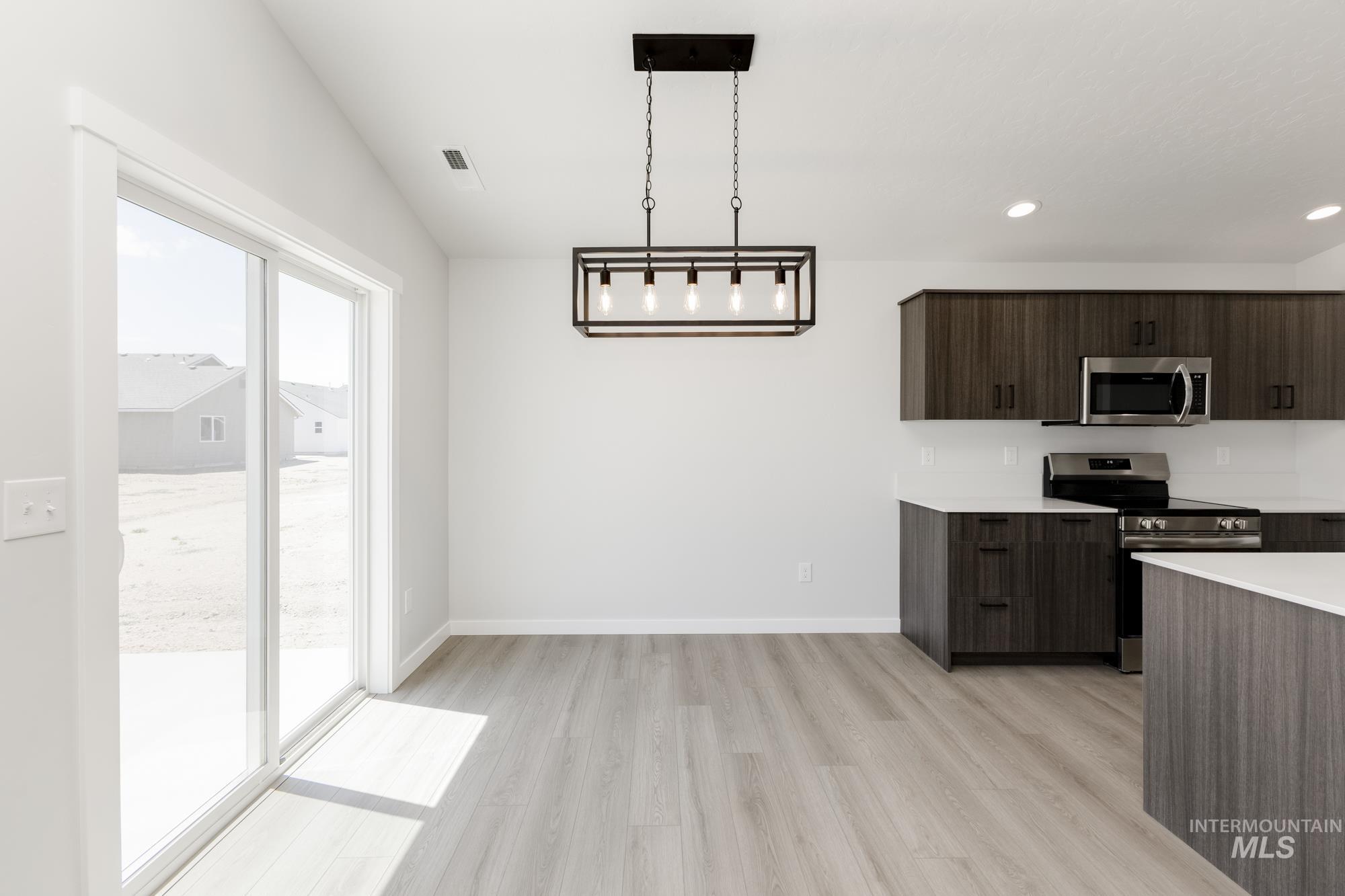 Kitchen featuring stainless steel appliances, light countertops, light wood finished floors, dark brown cabinets, and modern cabinets