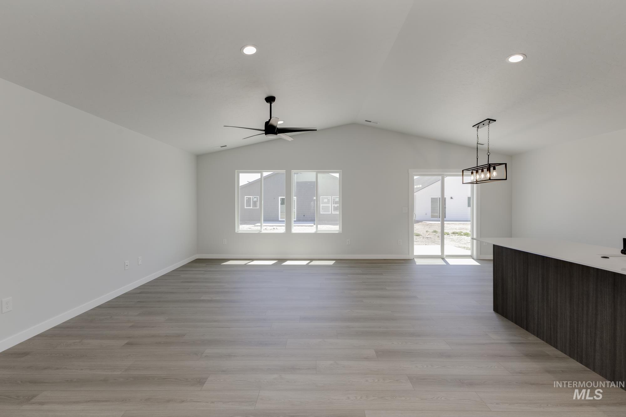Unfurnished living room featuring light wood-style floors, a ceiling fan, vaulted ceiling, recessed lighting, and a chandelier