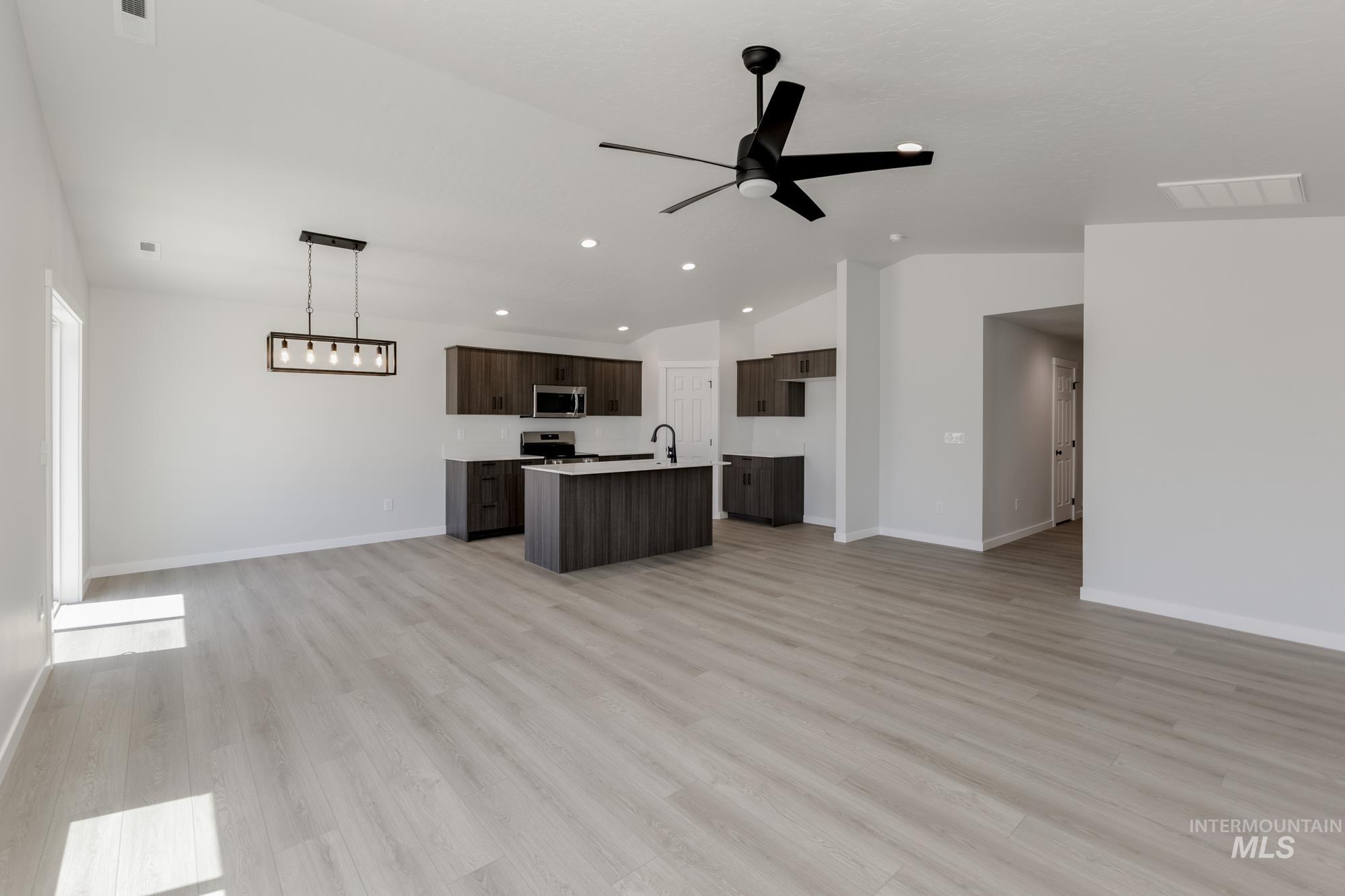 Kitchen featuring open floor plan, vaulted ceiling, dark brown cabinets, a center island with sink, and light wood-style flooring