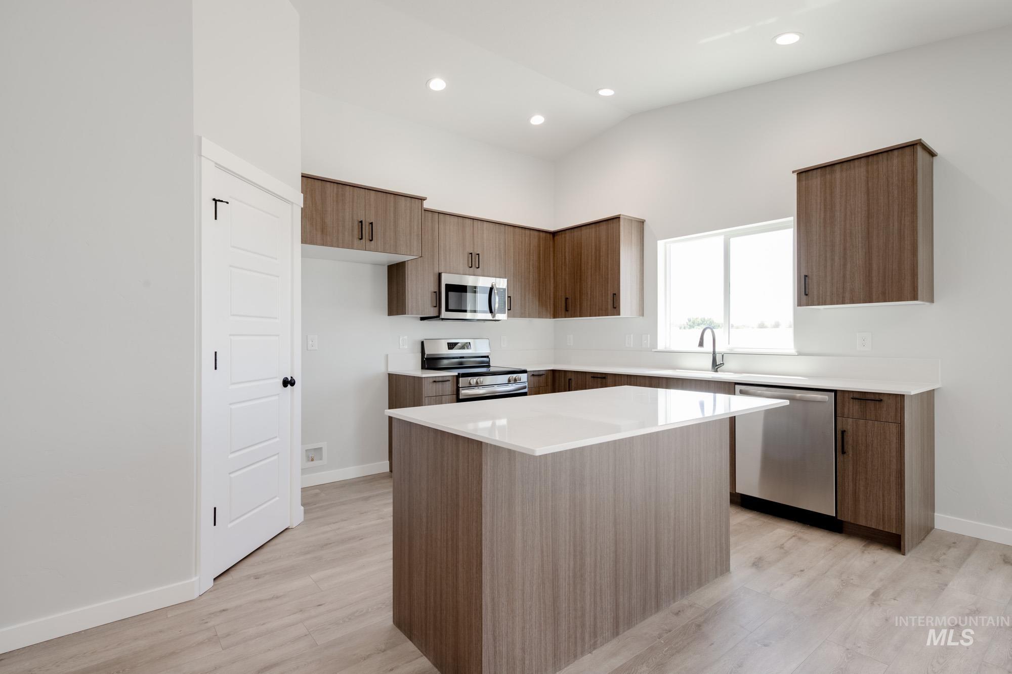 Kitchen featuring stainless steel appliances, light wood-style floors, a kitchen island, light countertops, and high vaulted ceiling