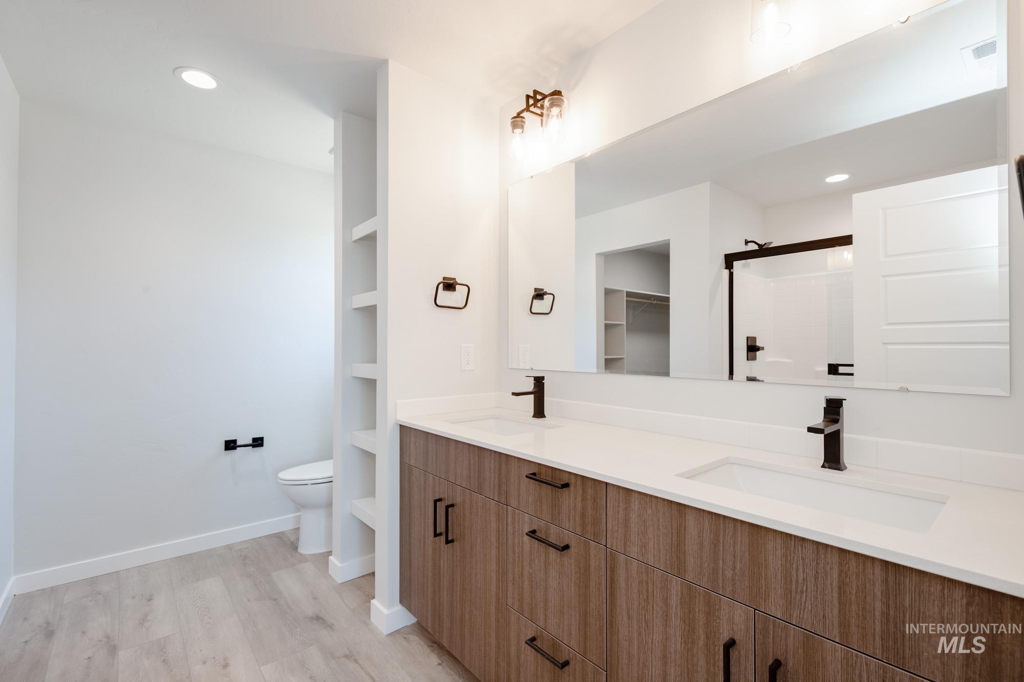 Full bath featuring double vanity, wood finished floors, an enclosed shower, and recessed lighting