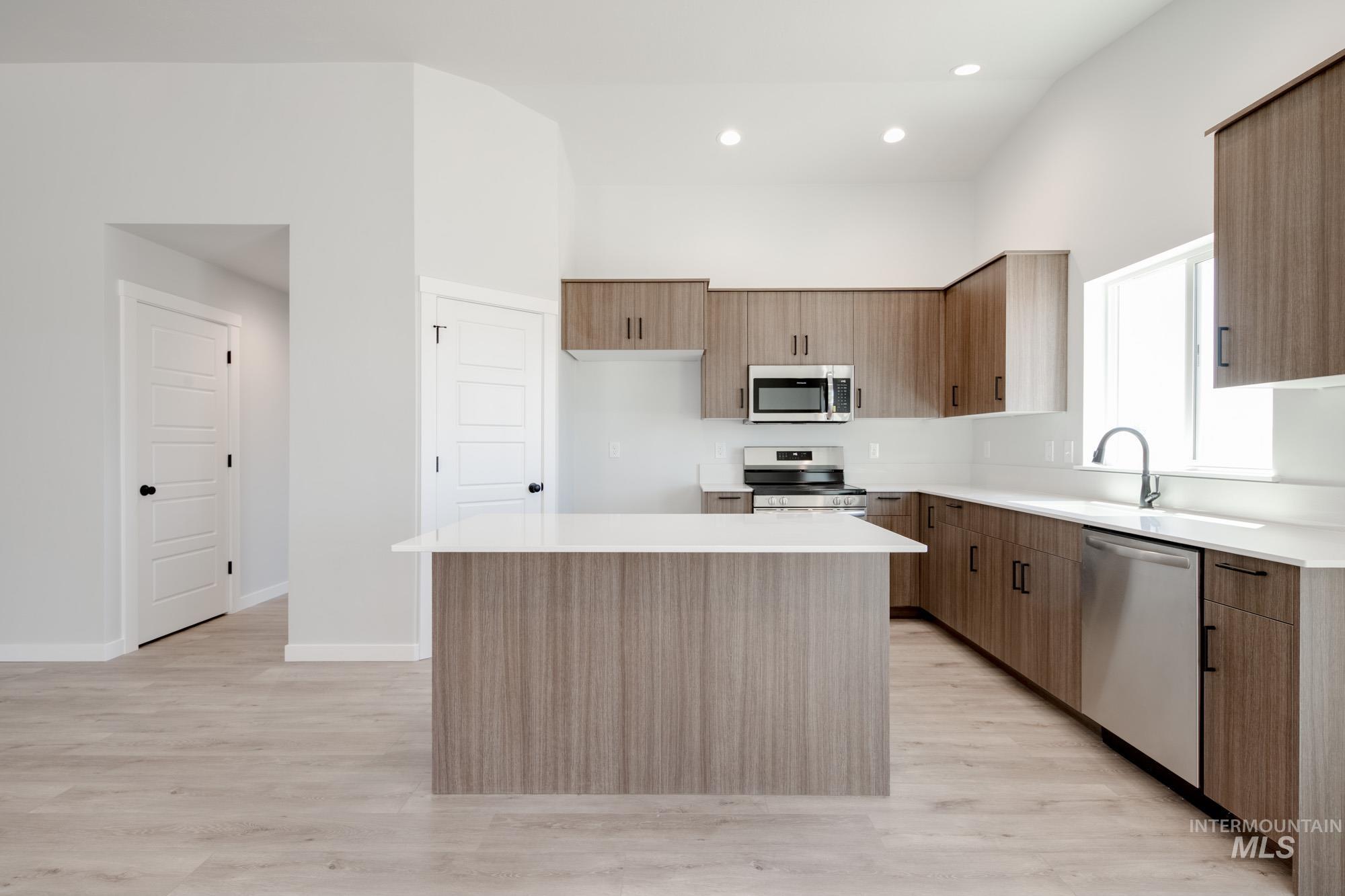 Kitchen featuring a center island, light wood-type flooring, stainless steel appliances, a towering ceiling, and light countertops