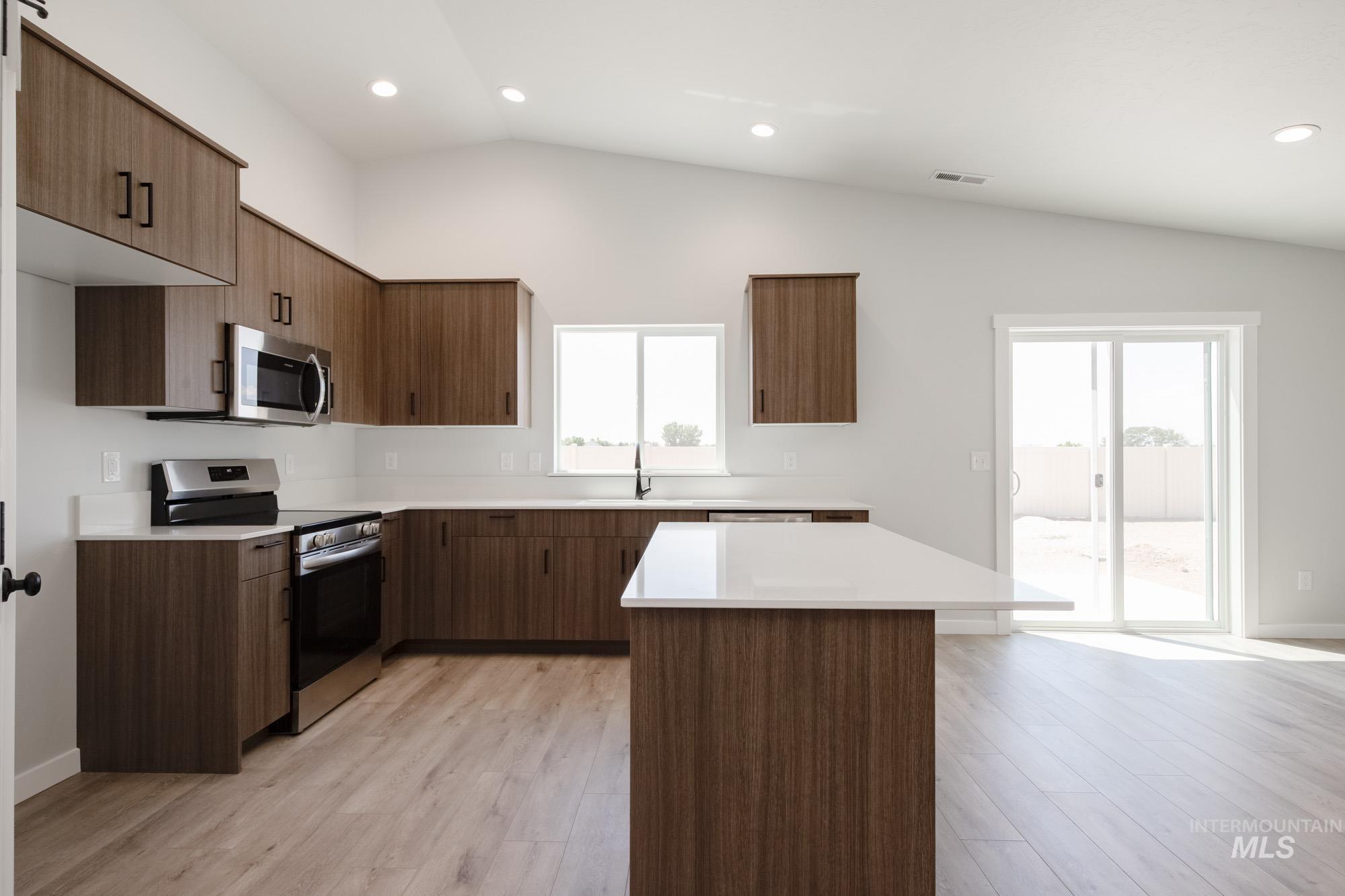 Kitchen featuring vaulted ceiling, stainless steel appliances, light countertops, light wood-type flooring, and recessed lighting