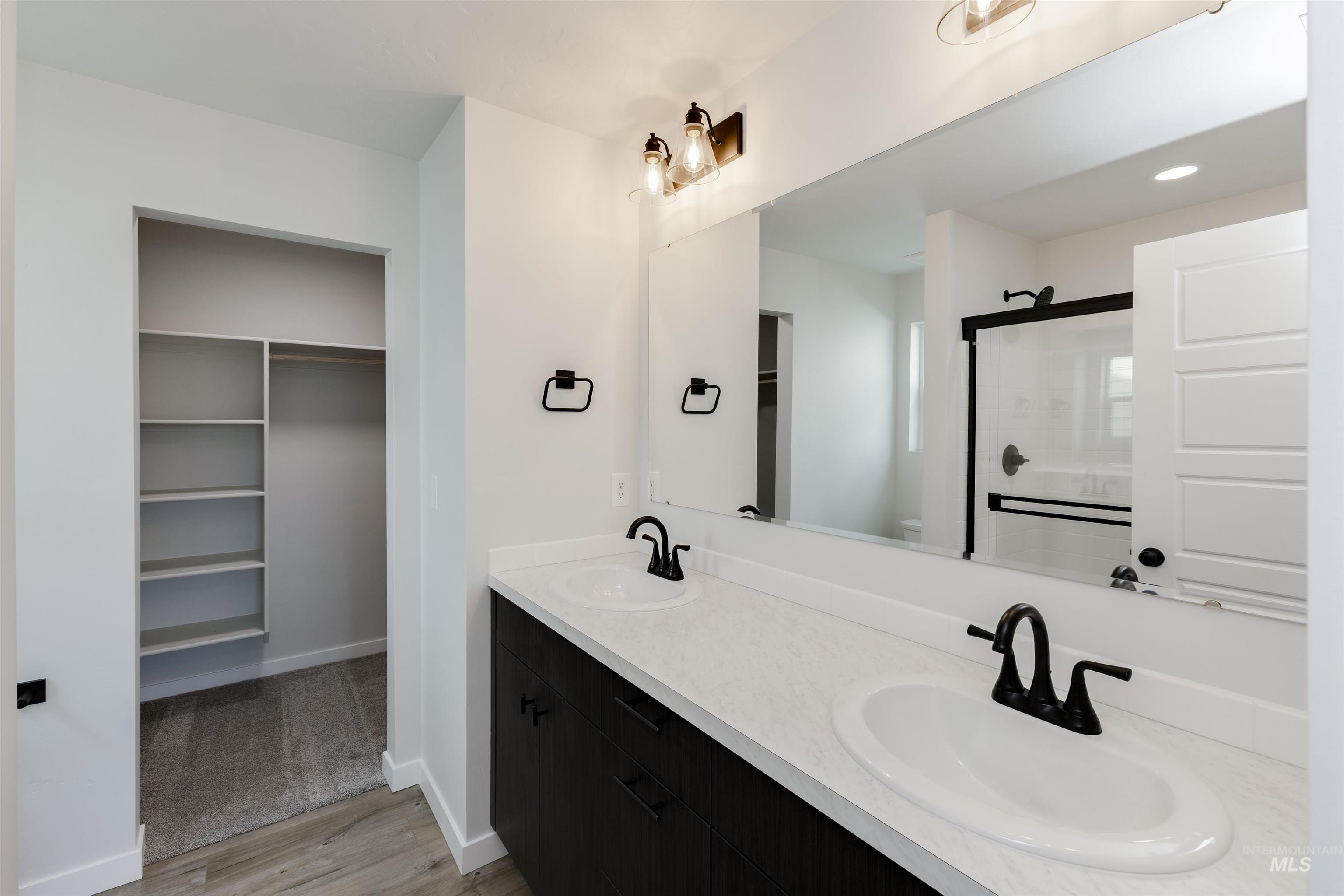 Full bathroom with double vanity, wood finished floors, a shower with door, and a walk in closet