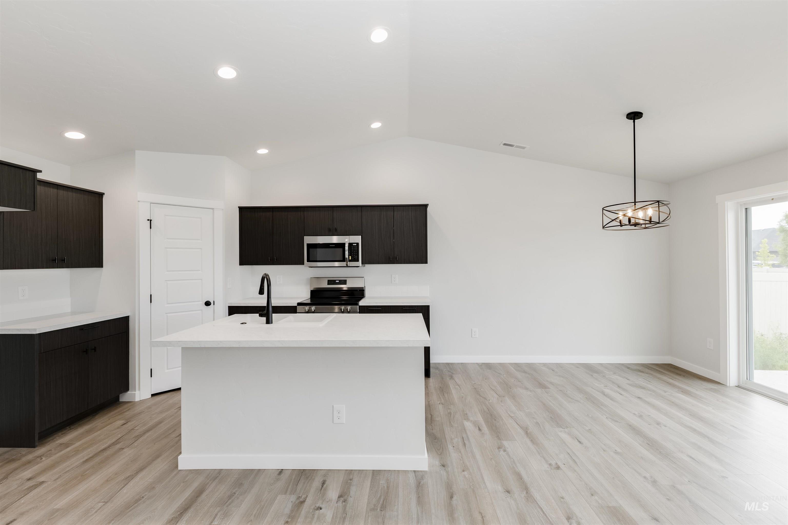 Kitchen with lofted ceiling, light wood-style flooring, light countertops, stainless steel appliances, and a kitchen island with sink