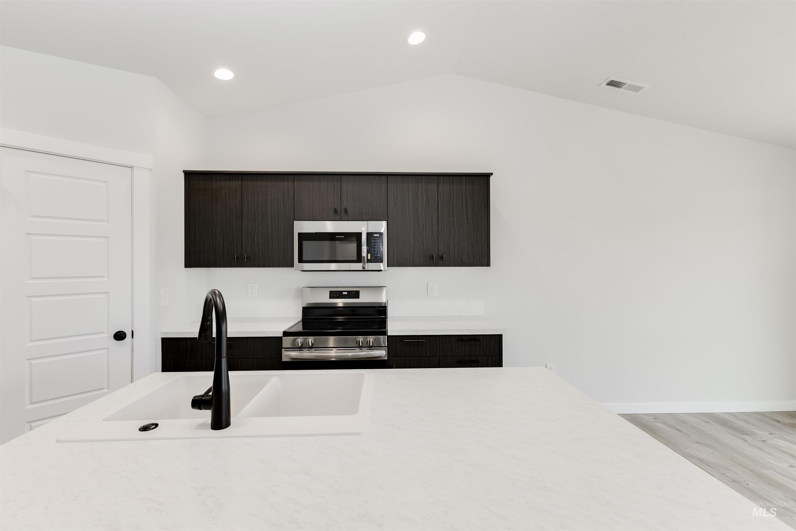 Kitchen featuring vaulted ceiling, stainless steel appliances, light countertops, light wood-style floors, and recessed lighting