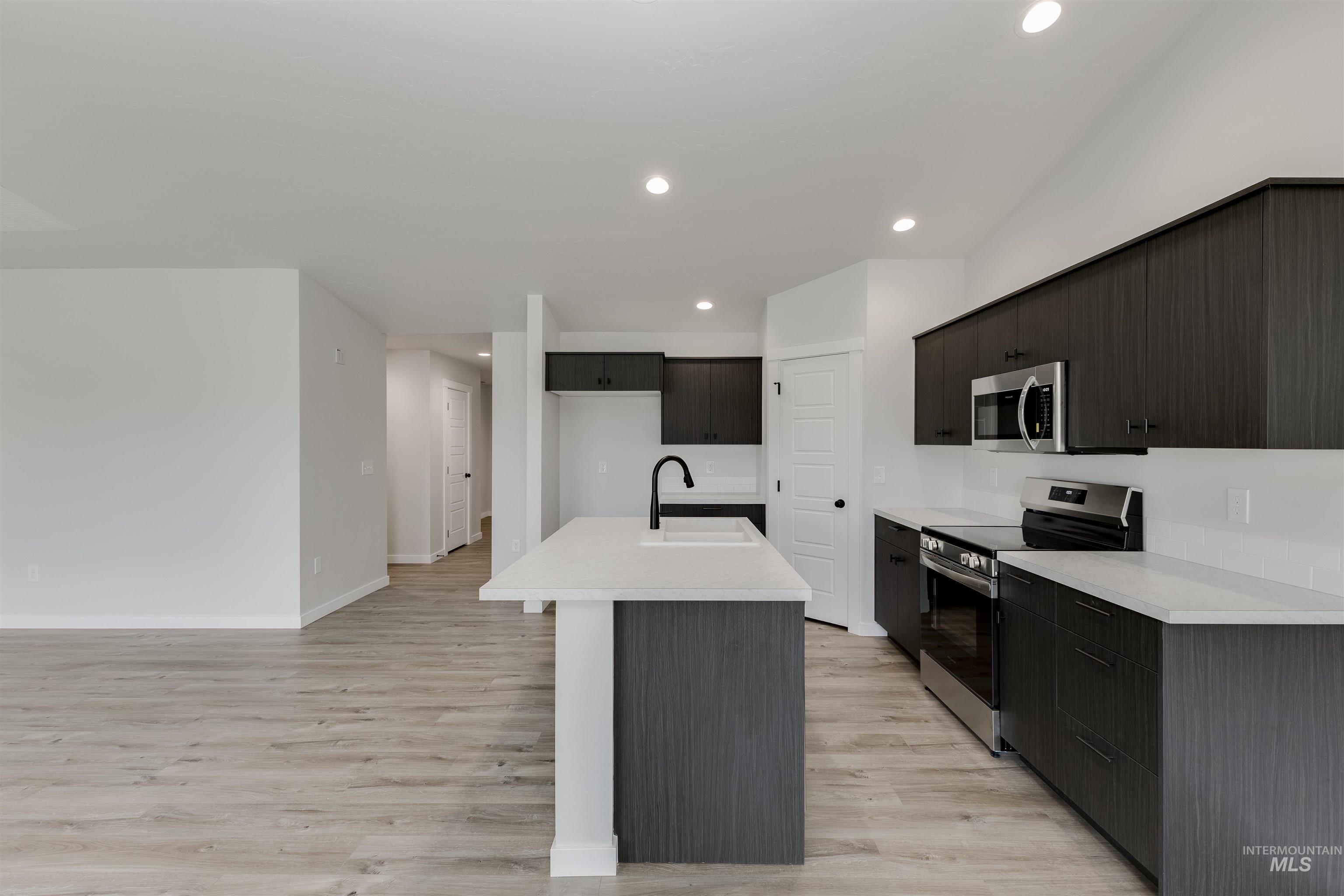 Kitchen featuring appliances with stainless steel finishes, light wood finished floors, light countertops, a center island with sink, and recessed lighting