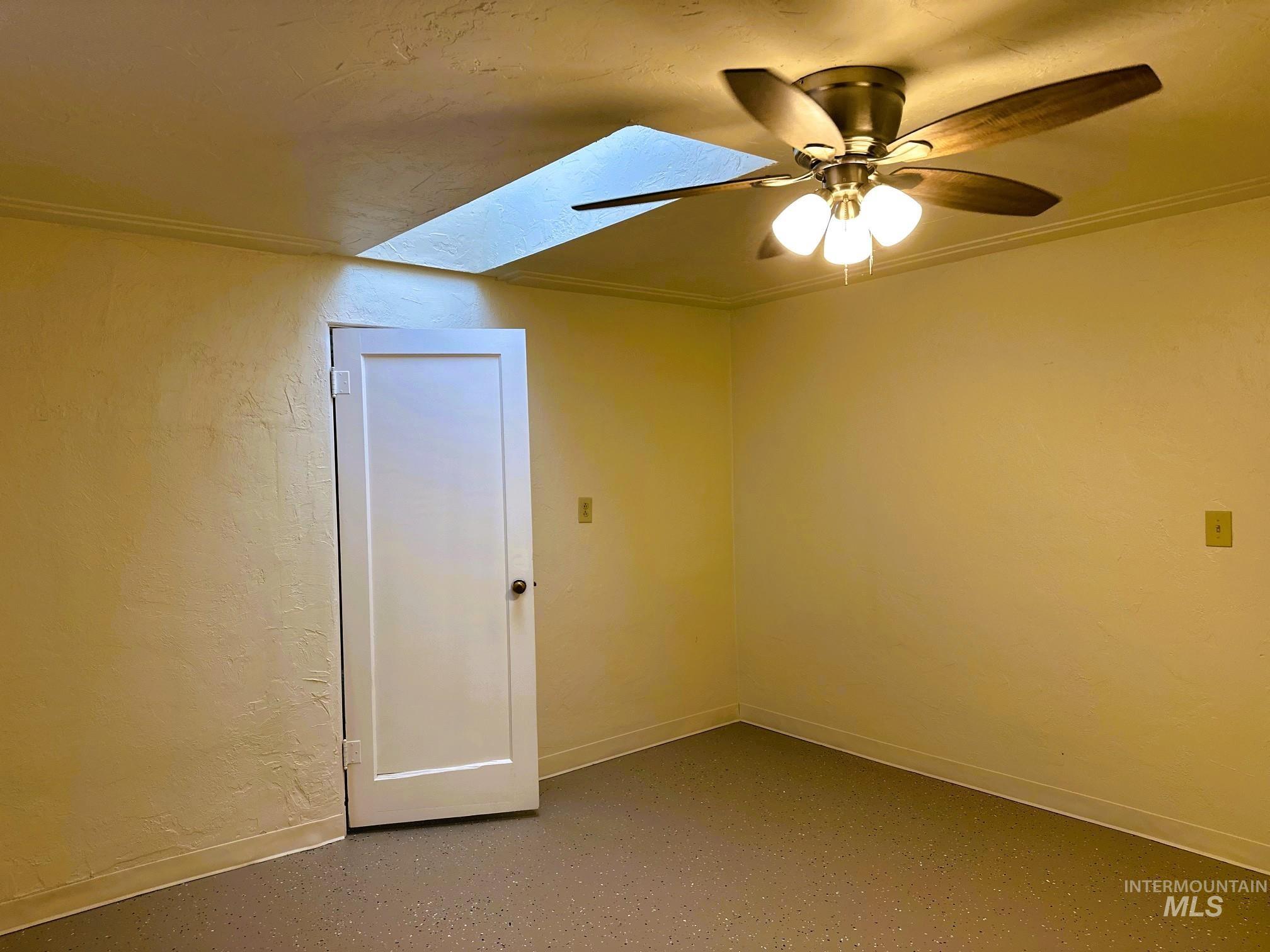 Spare room with a skylight, a textured wall, crown molding, ceiling fan, and concrete floors