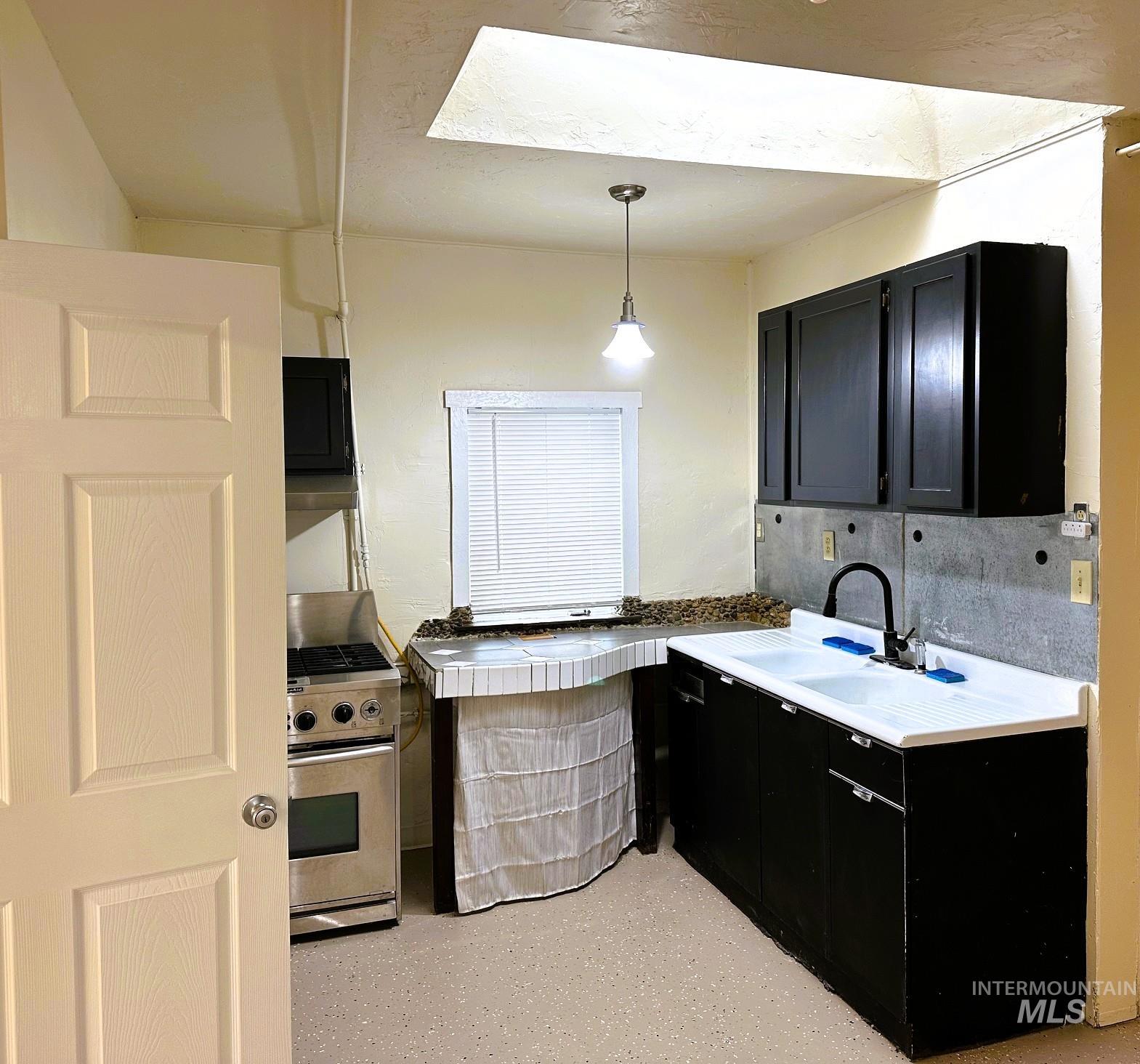 Kitchen featuring dark cabinetry, hanging light fixtures, a skylight, and stainless steel gas range