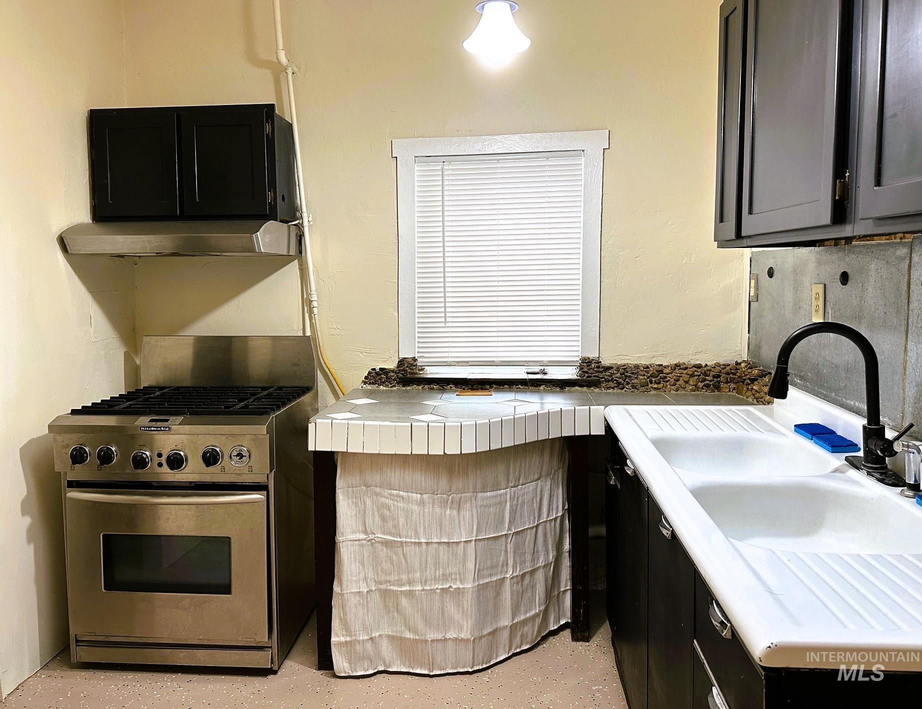 Kitchen featuring dark cabinets, stainless steel range with gas stovetop, tile countertops, and under cabinet range hood