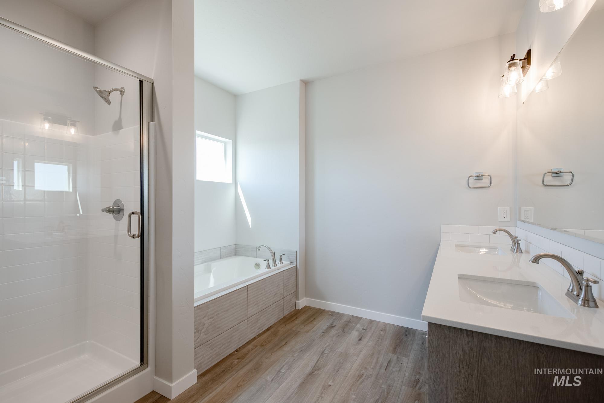 Full bathroom with a garden tub, light wood-style flooring, a stall shower, and double vanity