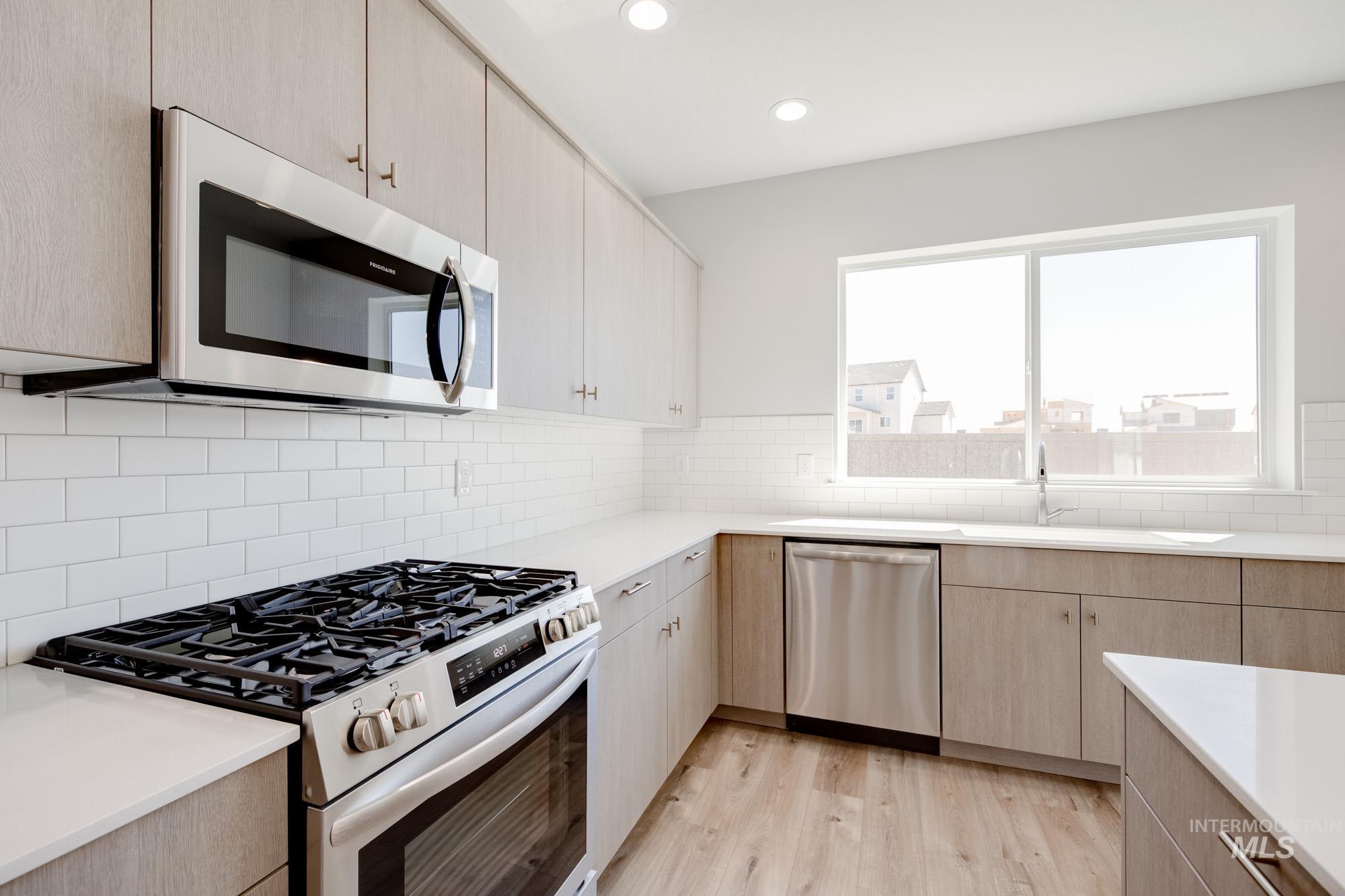 Kitchen featuring light brown cabinetry, stainless steel appliances, light wood finished floors, recessed lighting, and decorative backsplash