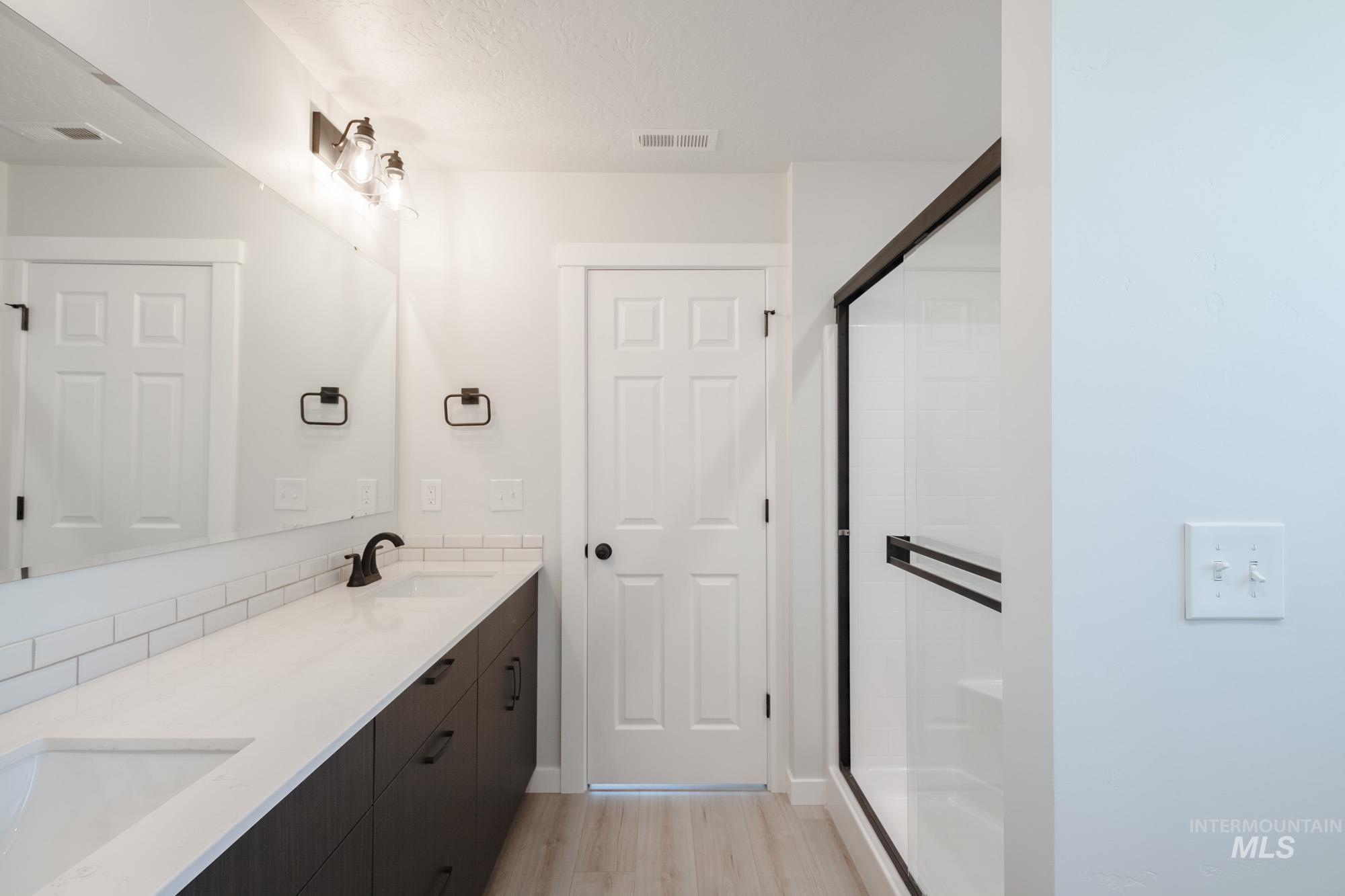 Bathroom featuring a stall shower, double vanity, light wood-style floors, and a textured ceiling