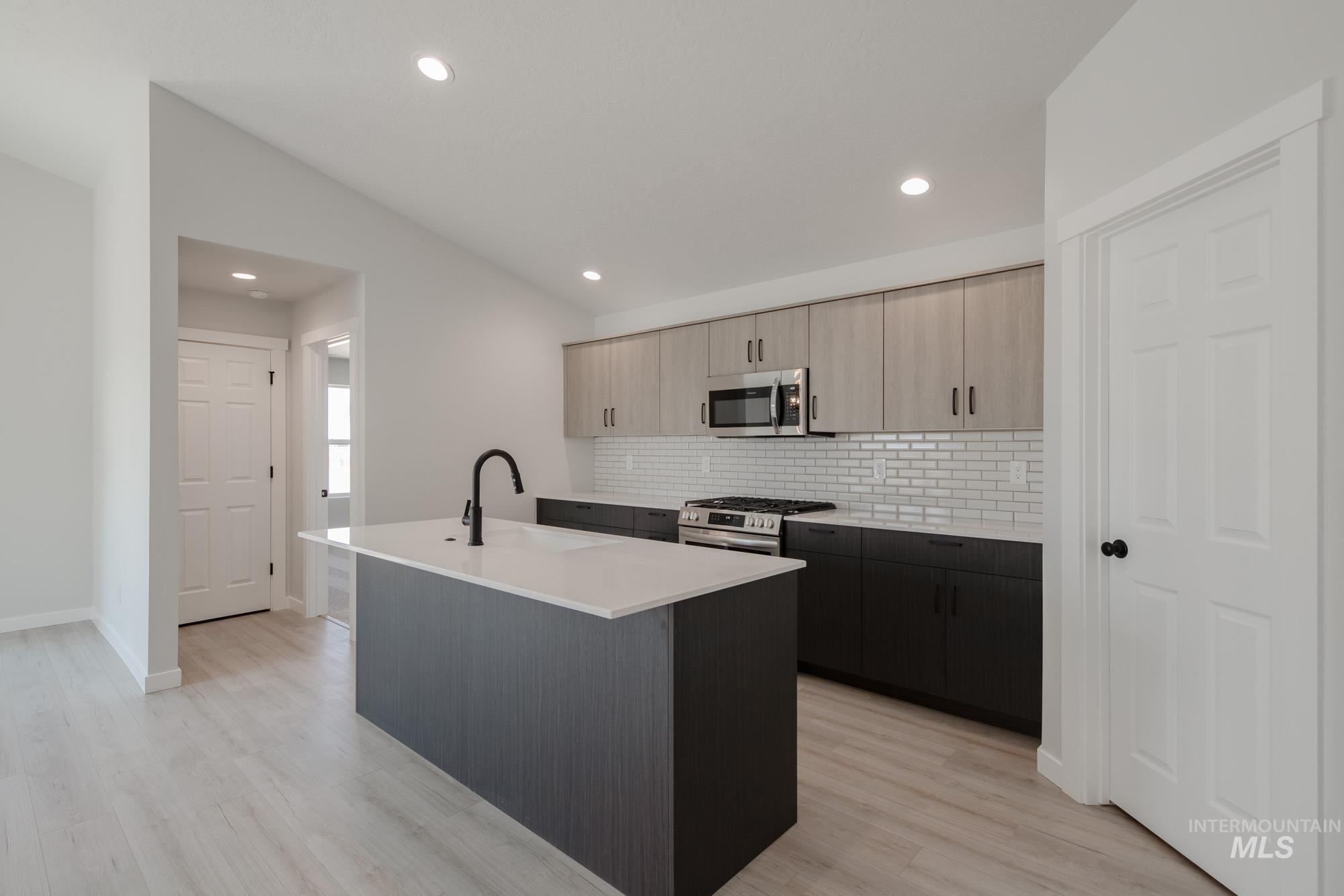 Kitchen featuring an island with sink, tasteful backsplash, stainless steel appliances, light stone countertops, and light wood-style flooring