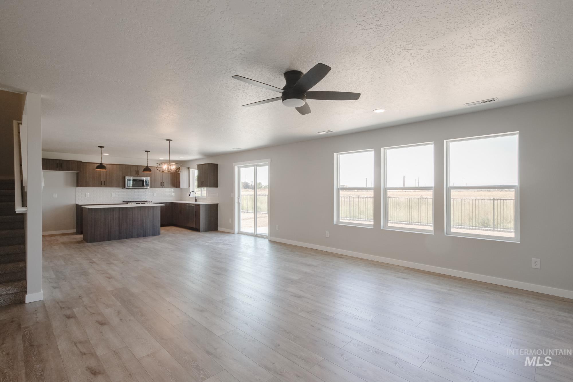 Unfurnished living room with light wood-type flooring, a textured ceiling, ceiling fan, and stairway