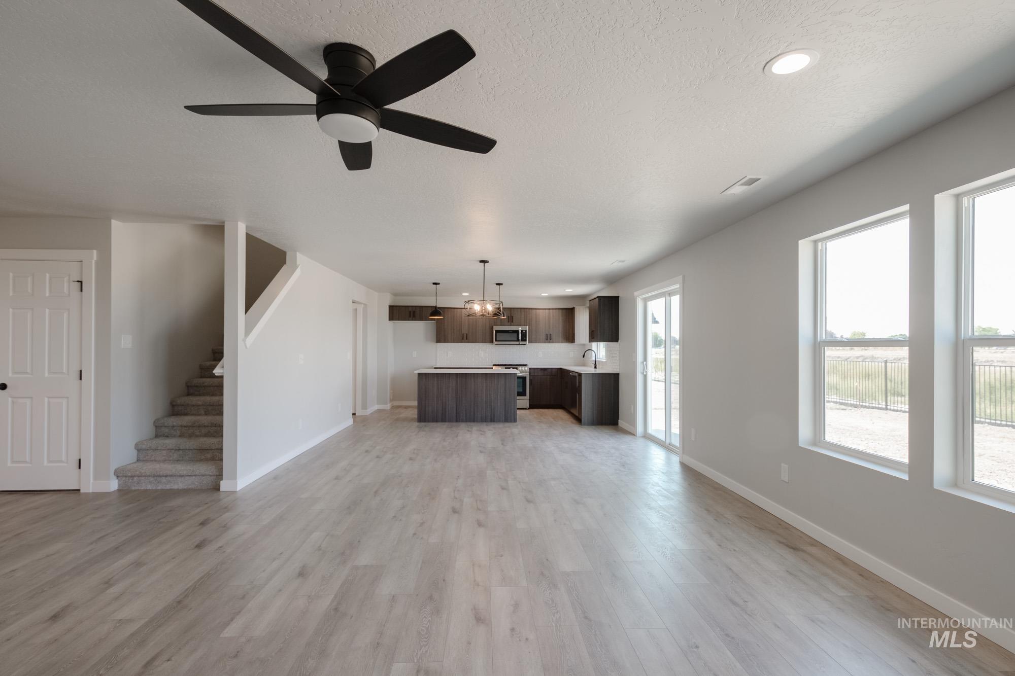 Unfurnished living room featuring light wood-type flooring, a ceiling fan, a textured ceiling, stairway, and recessed lighting