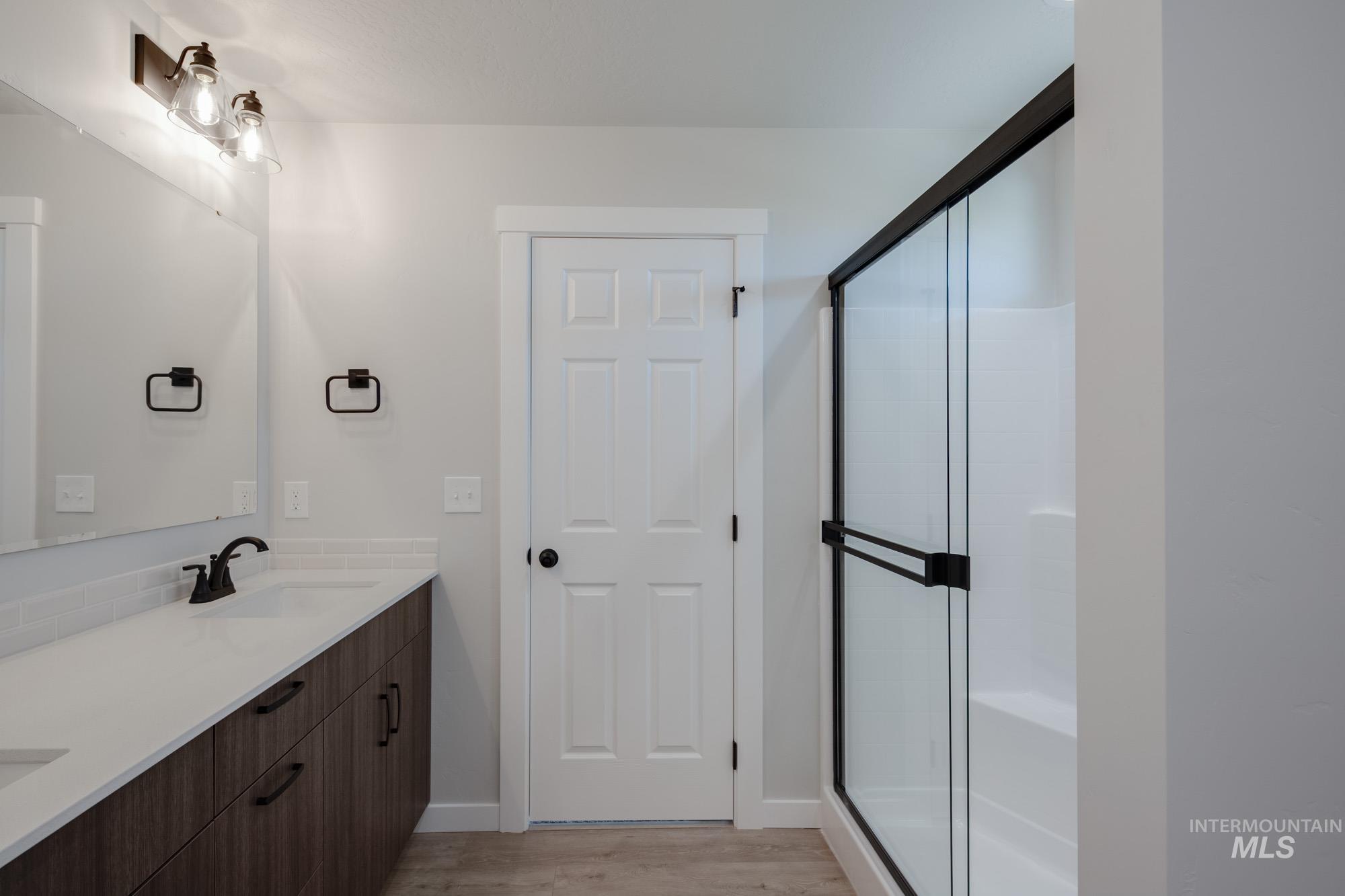 Bathroom with light wood-type flooring, double vanity, and a shower stall