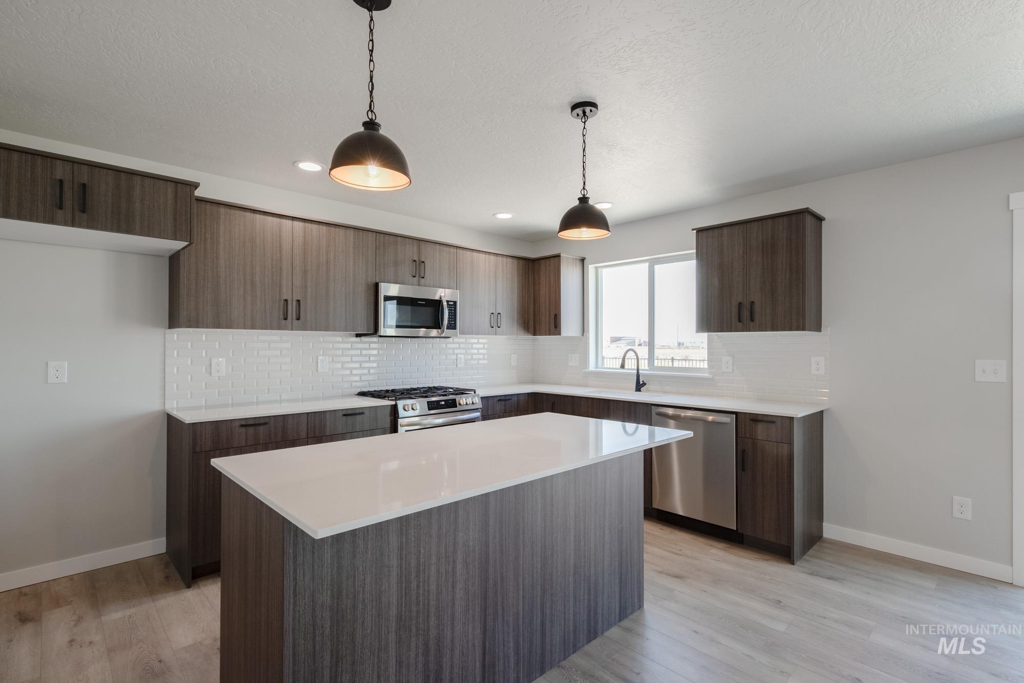 Kitchen with hanging light fixtures, decorative backsplash, stainless steel appliances, light wood-type flooring, and recessed lighting