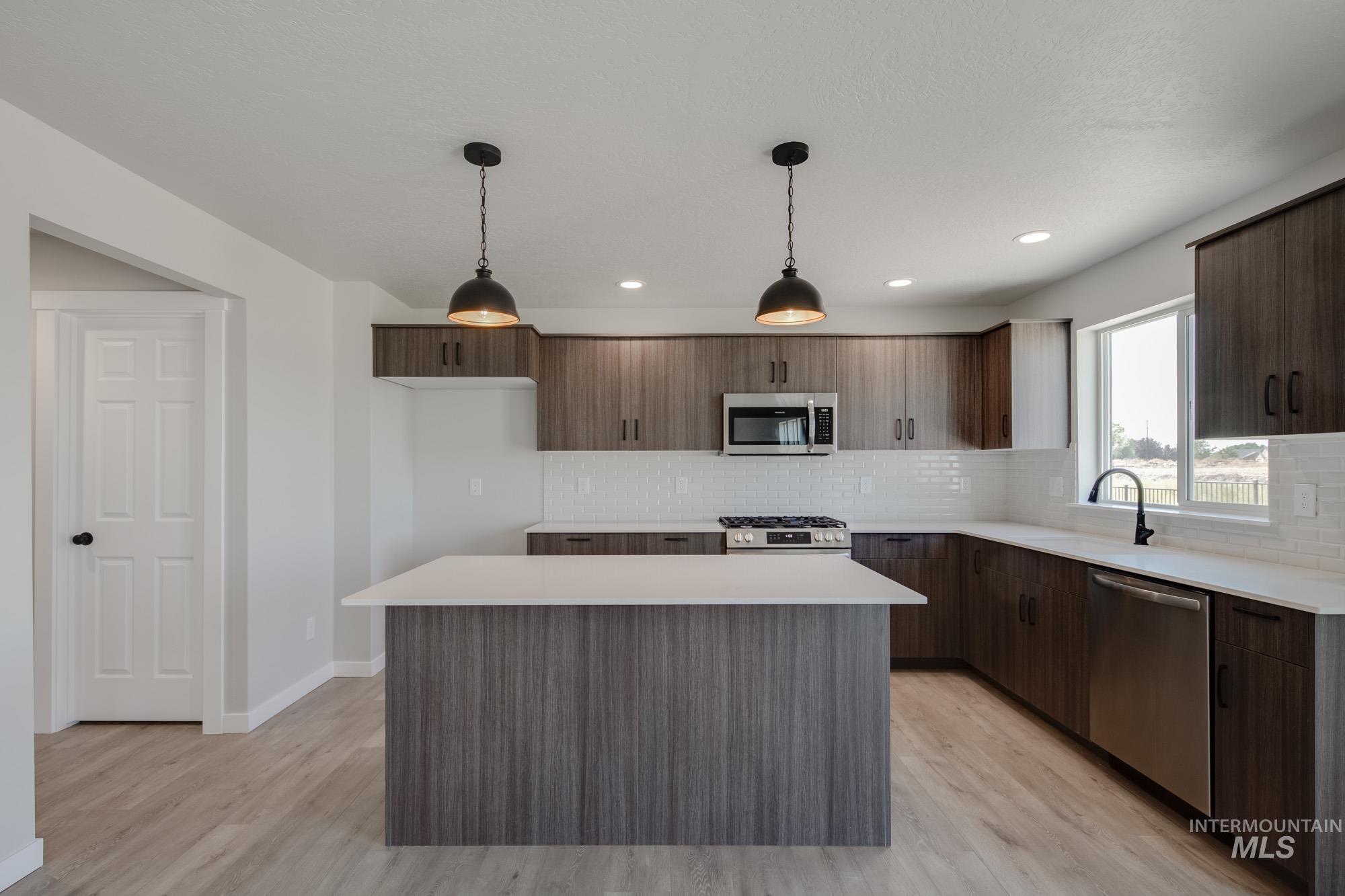 Kitchen with tasteful backsplash, decorative light fixtures, modern cabinets, appliances with stainless steel finishes, and recessed lighting